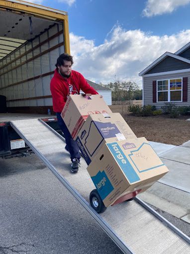 A man is pushing a large cardboard box on a dolly.