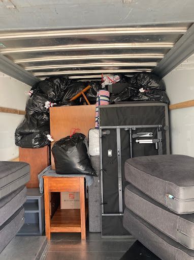 The inside of a moving truck filled with furniture and trash bags.