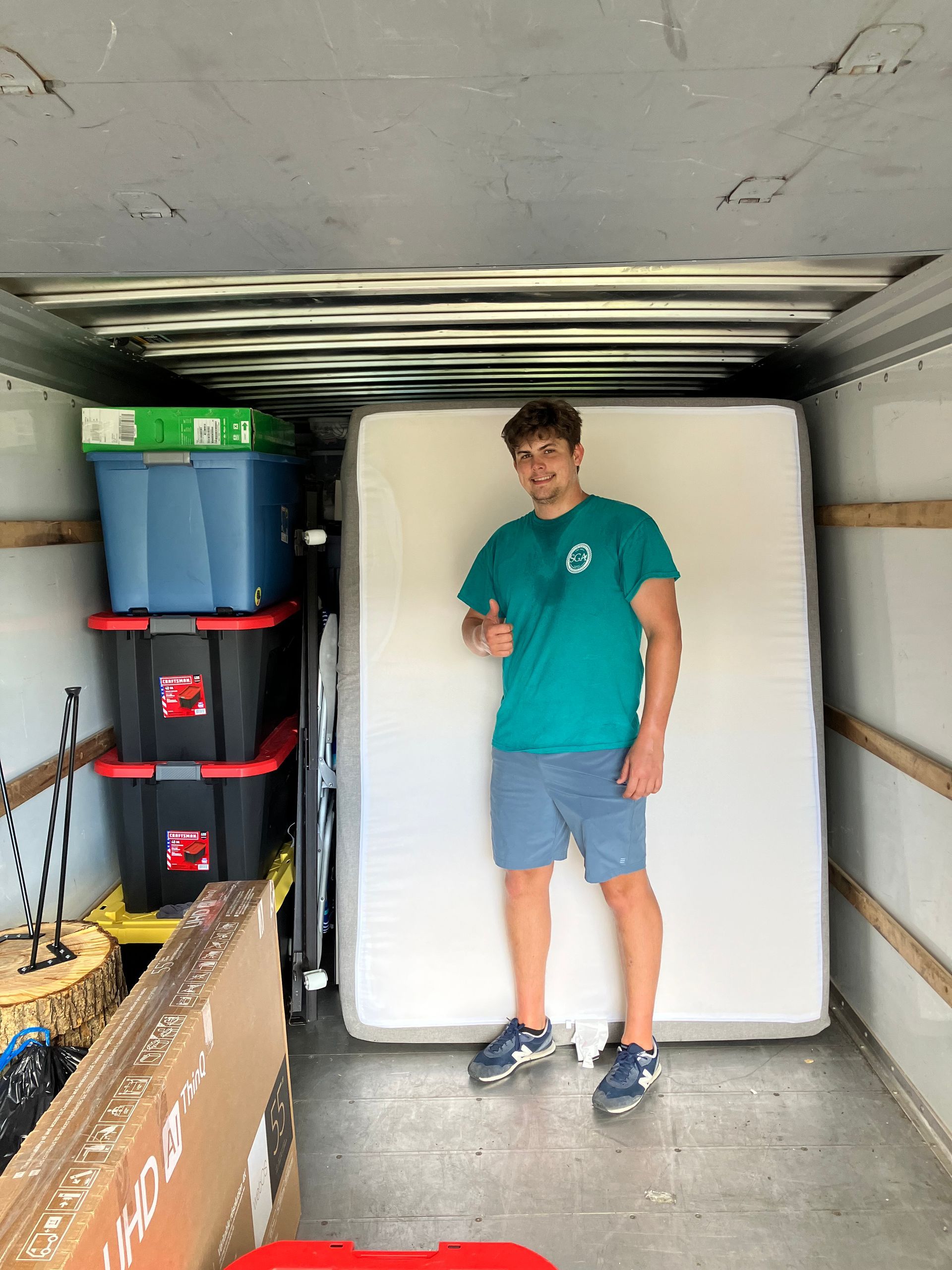 A man in a green shirt is standing next to a mattress in a truck.