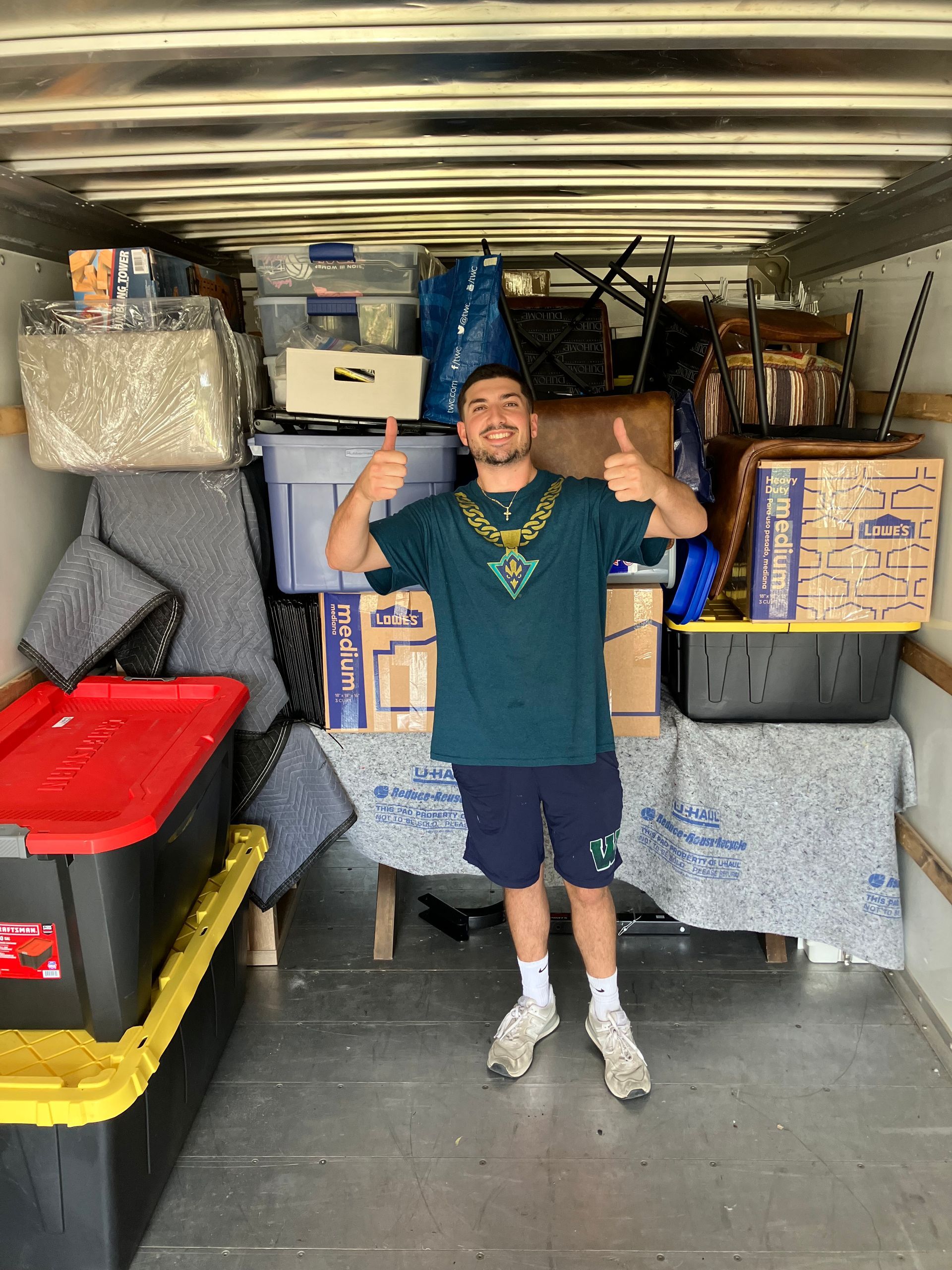 A man is standing in the back of a truck filled with boxes and giving a thumbs up.