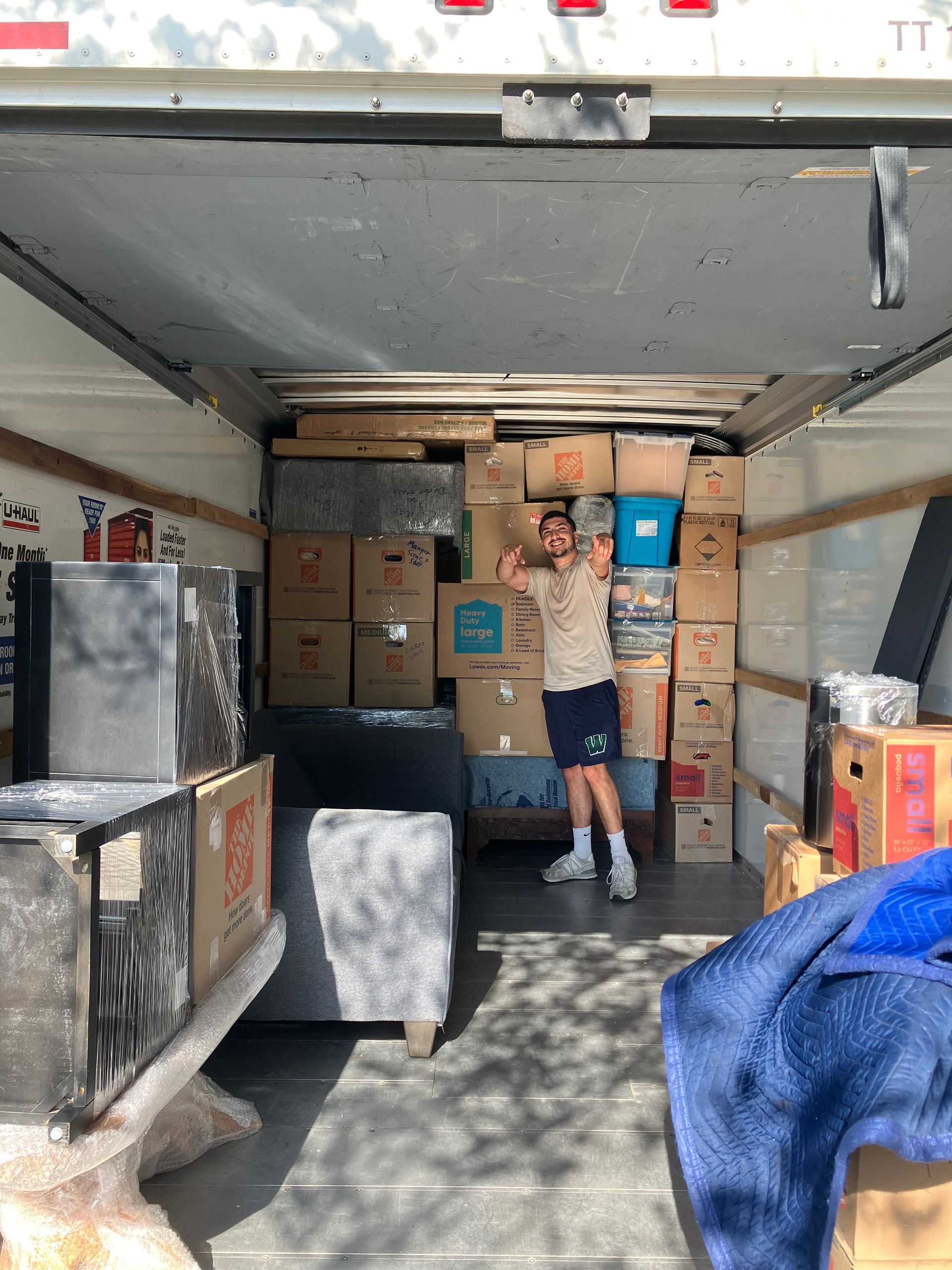 A man is standing in the back of a moving truck filled with boxes.
