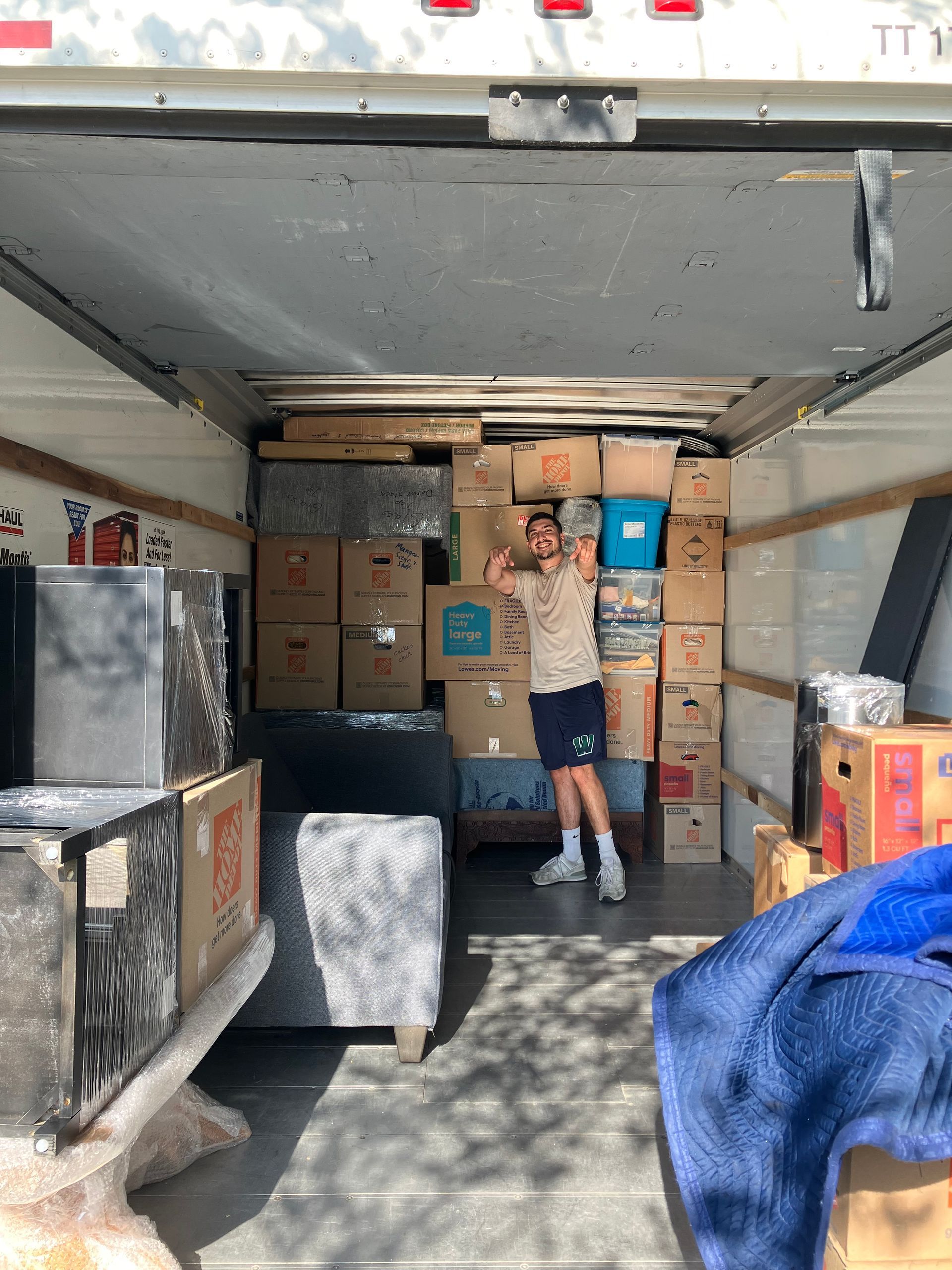 A man is standing in the back of a moving truck filled with boxes.