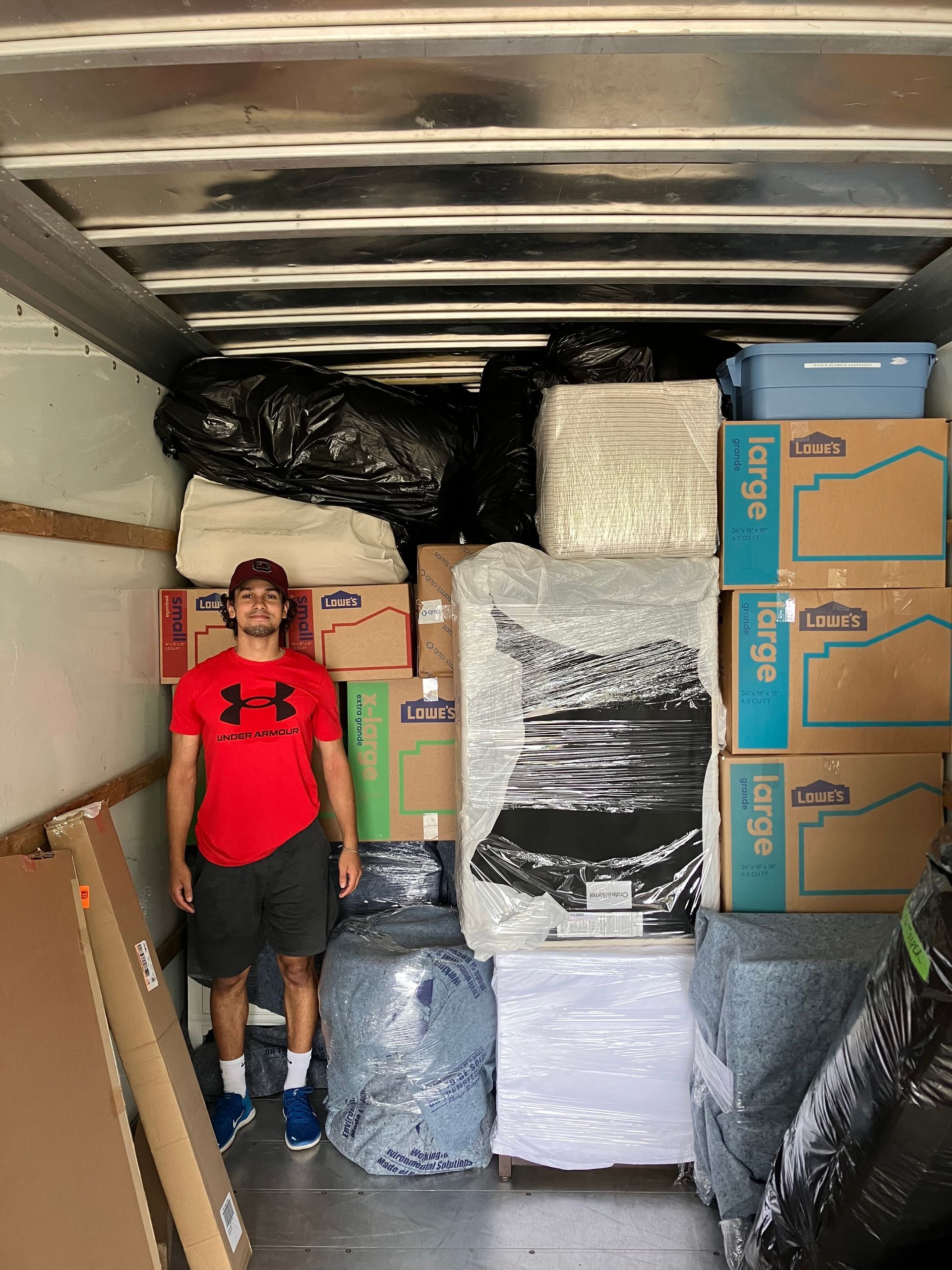 A man is standing in the back of a moving truck filled with boxes.