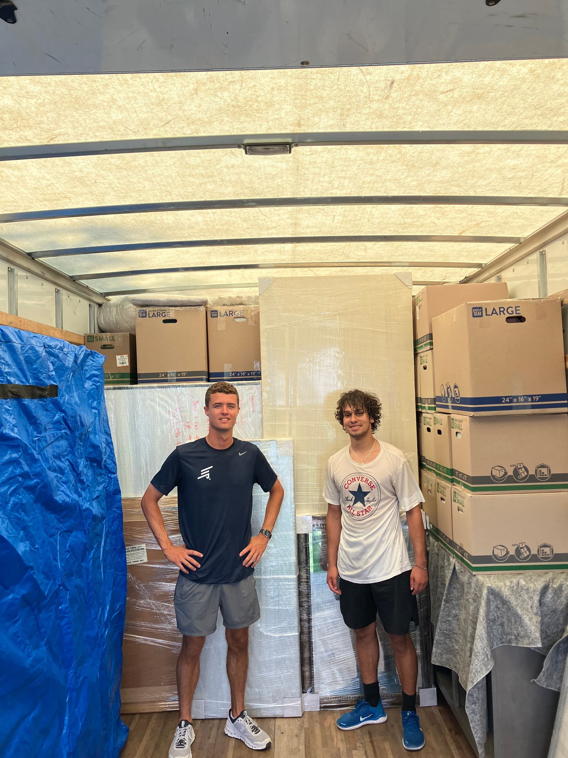 Two men are standing in the back of a truck filled with boxes.