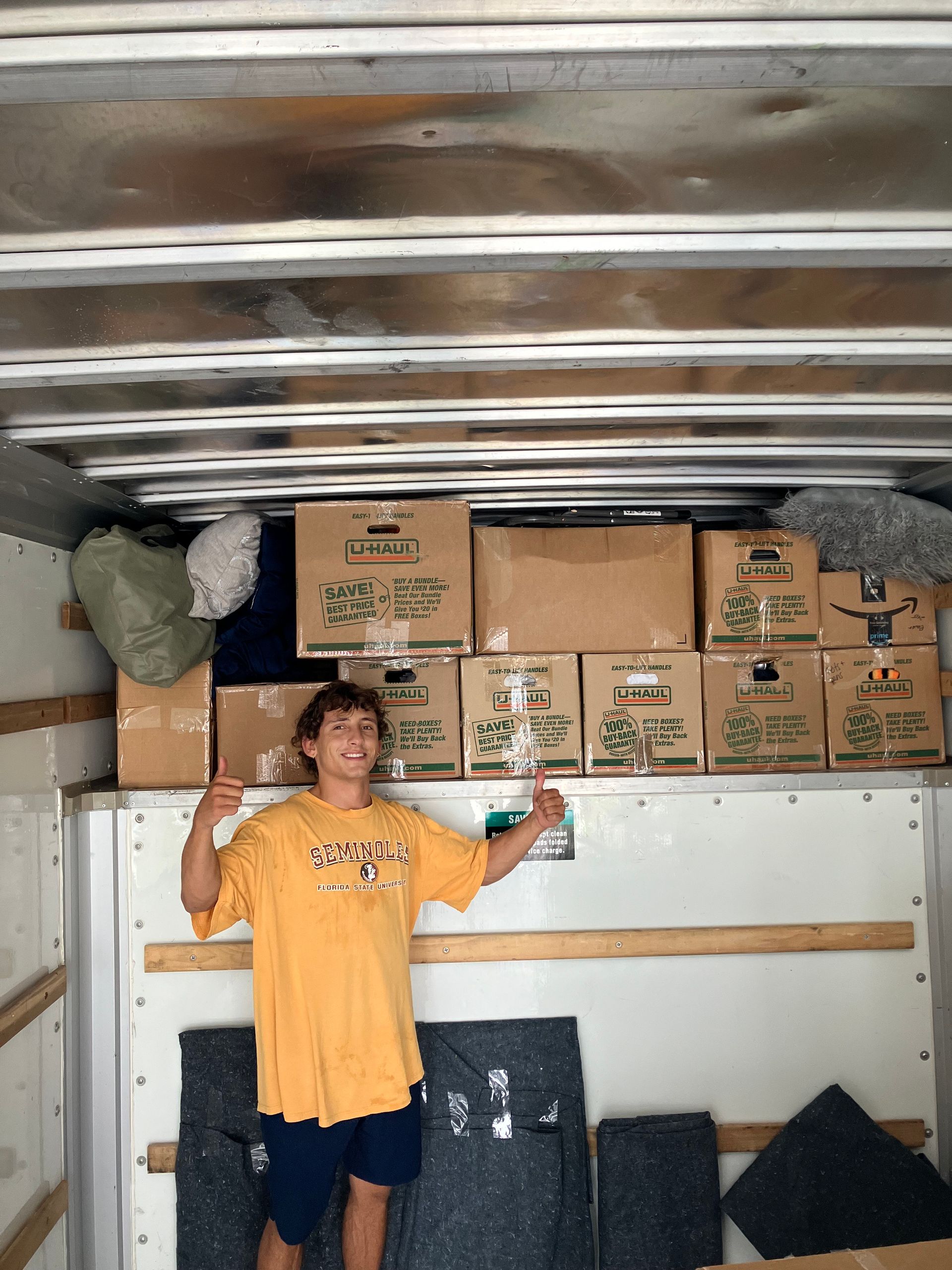 A man in a yellow shirt is standing in the back of a moving truck.
