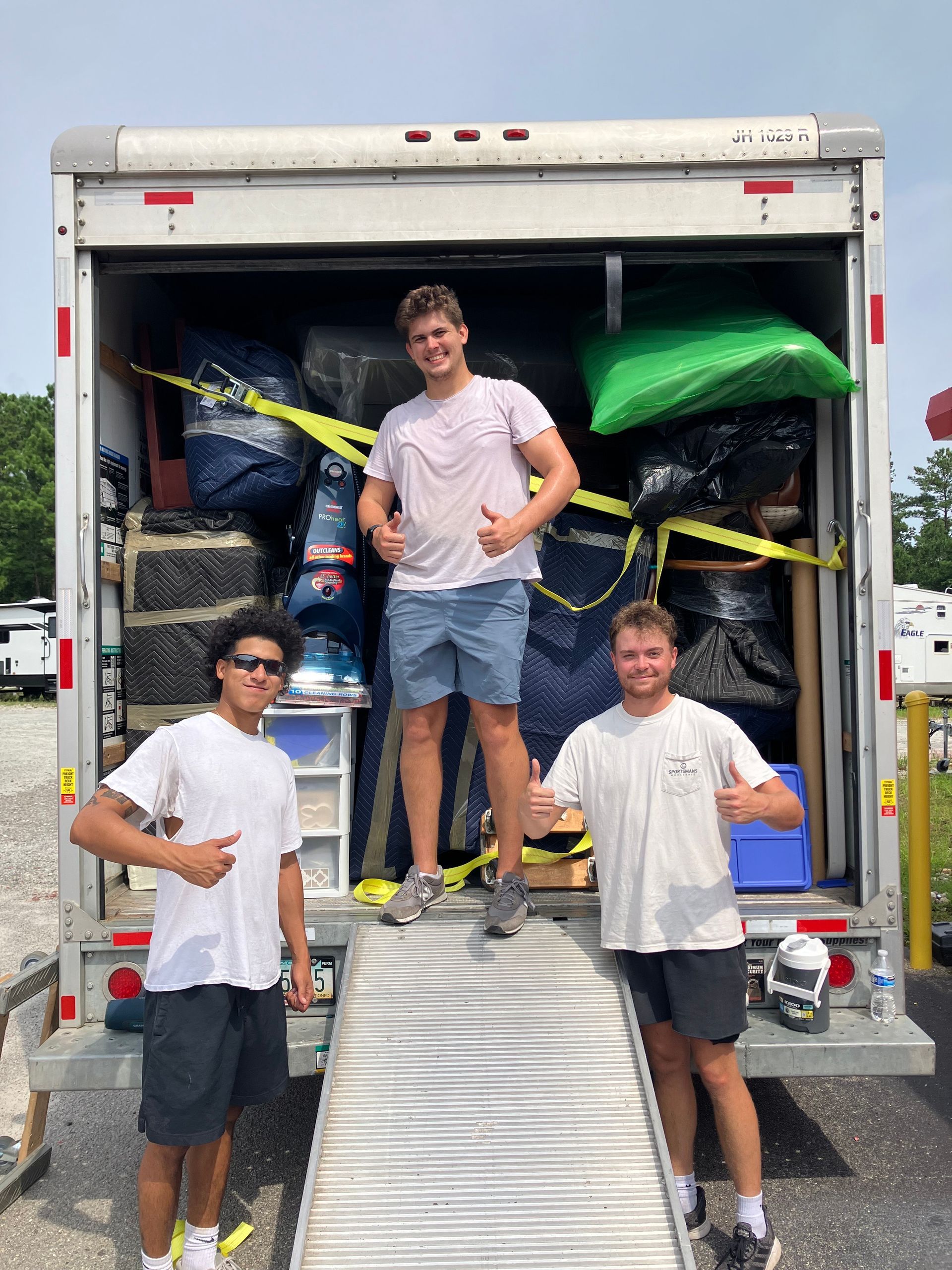 Three young men are standing in front of a moving truck.