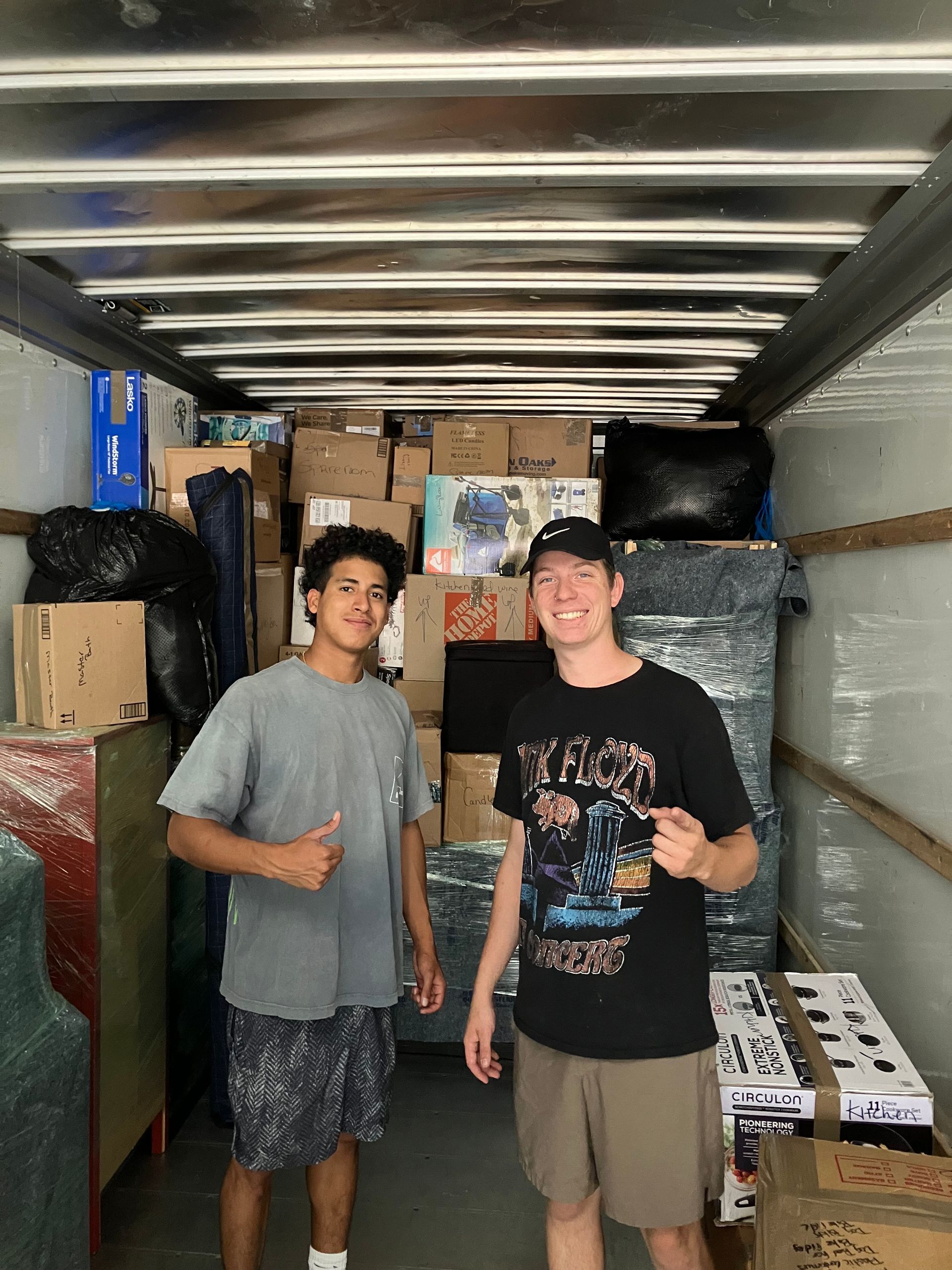 Two men are standing in the back of a truck filled with boxes.