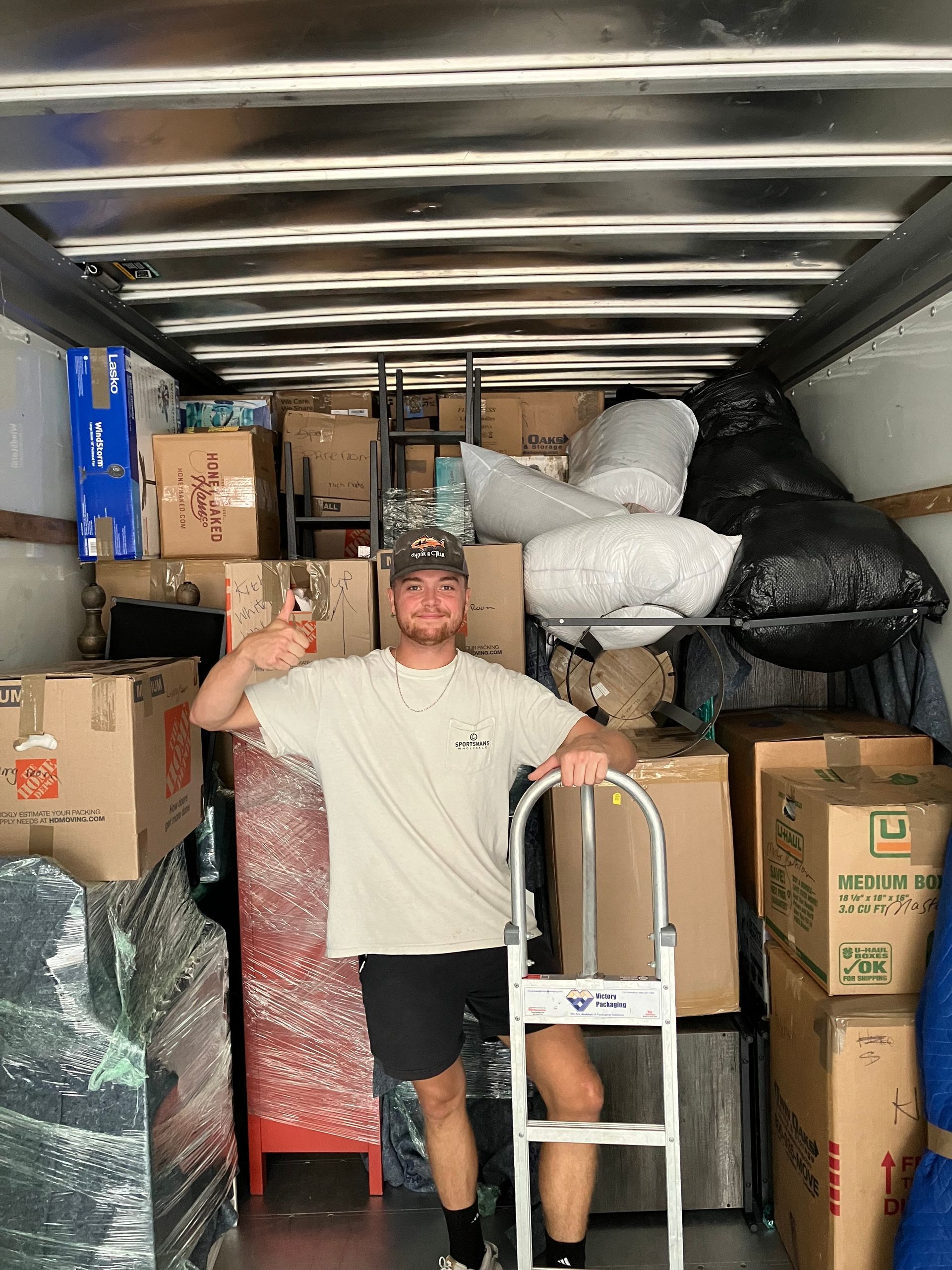 A man is standing in the back of a moving truck filled with boxes.