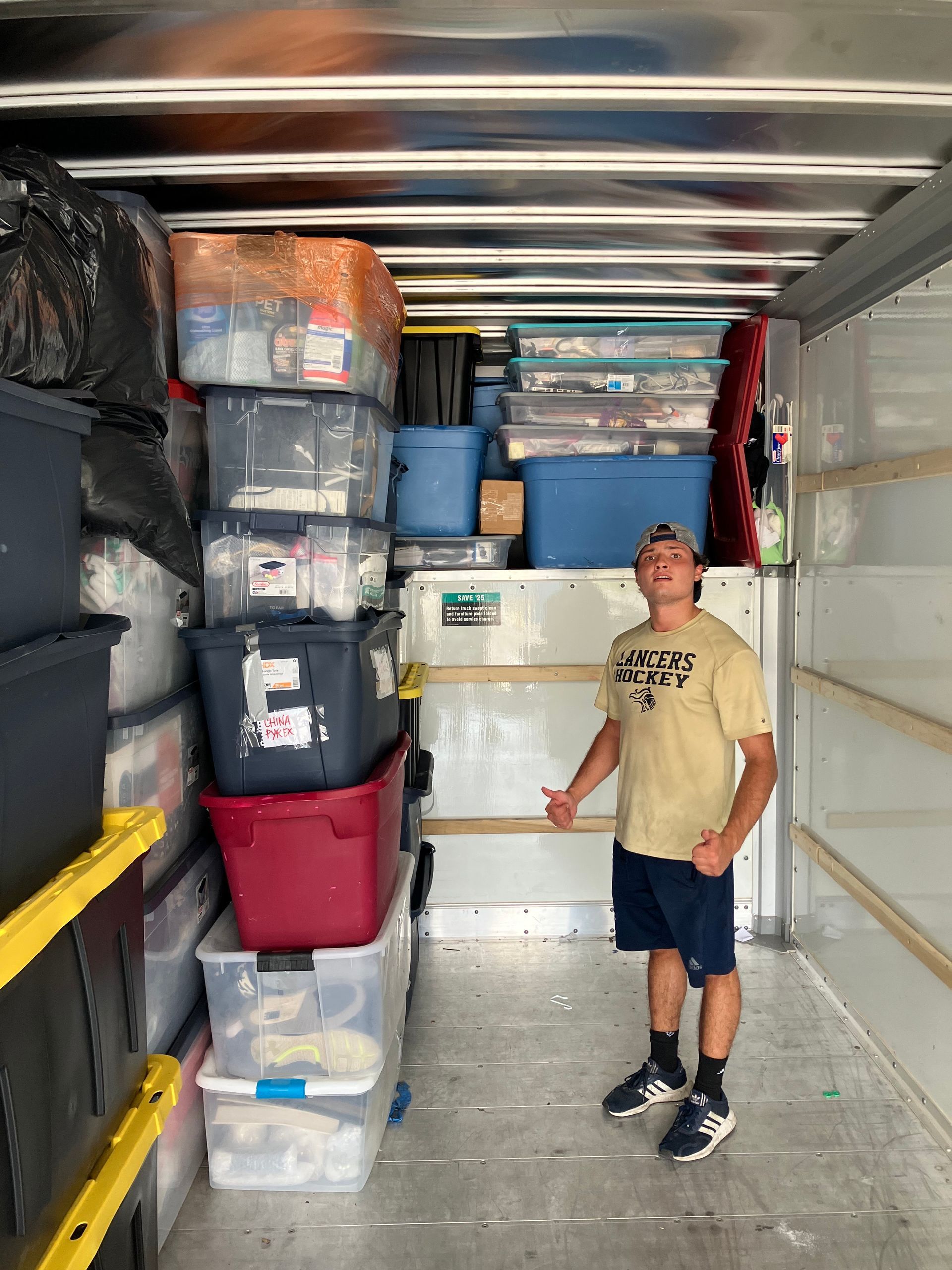 A man is standing in the back of a moving truck filled with boxes.
