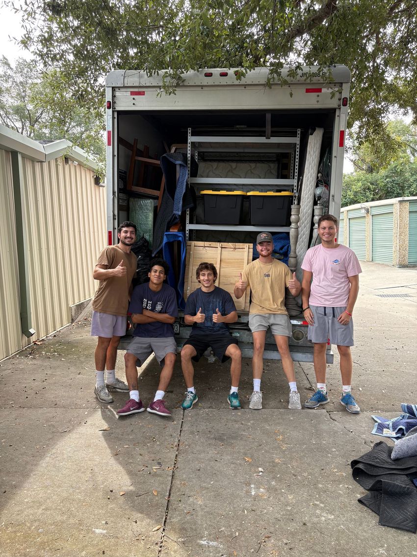 A group of young men are standing in front of a moving truck.