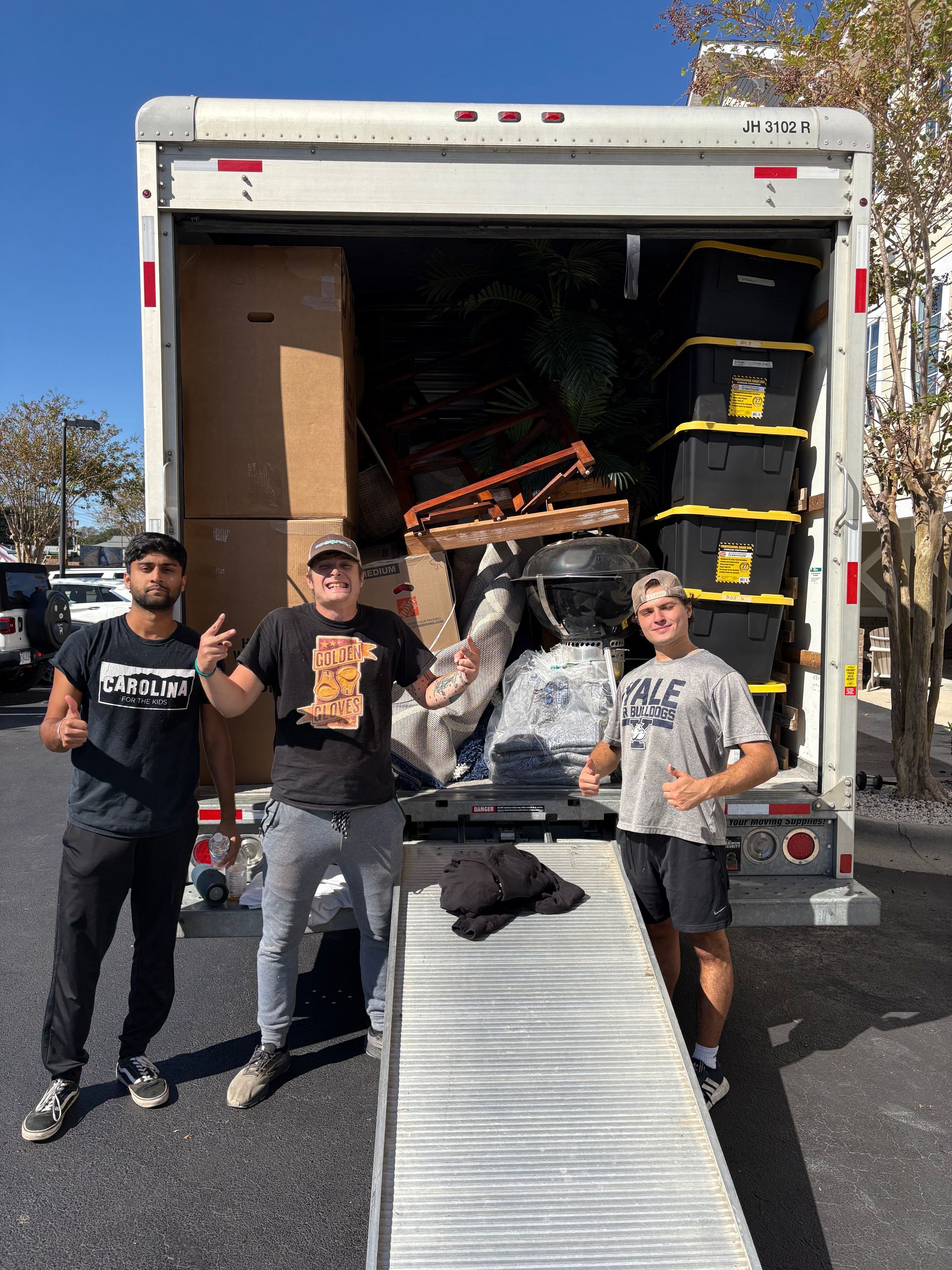 Three men are standing in front of a moving truck.