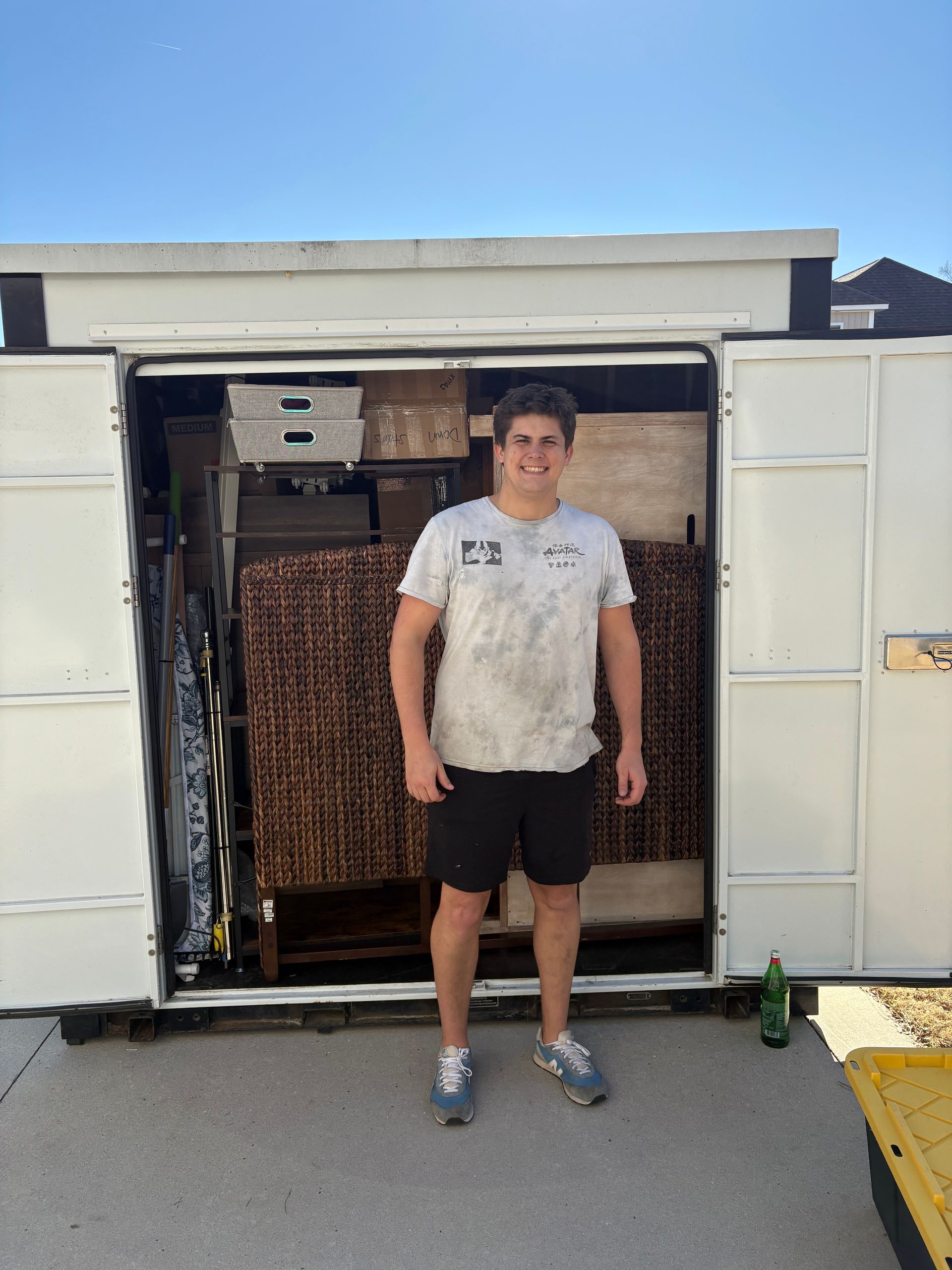 A man in a white shirt is standing in front of a white shed