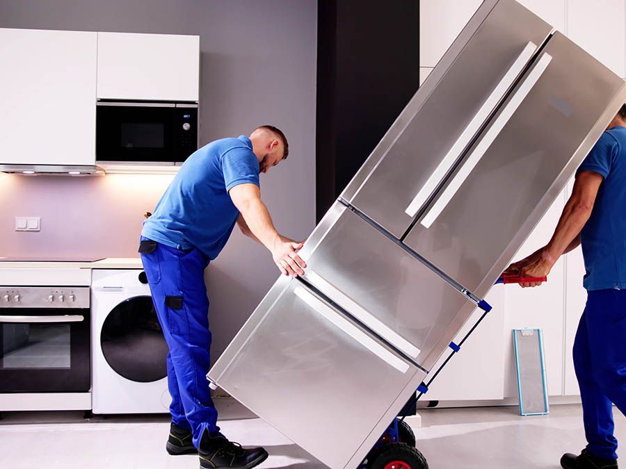 Two men are carrying a refrigerator on a dolly in a kitchen.