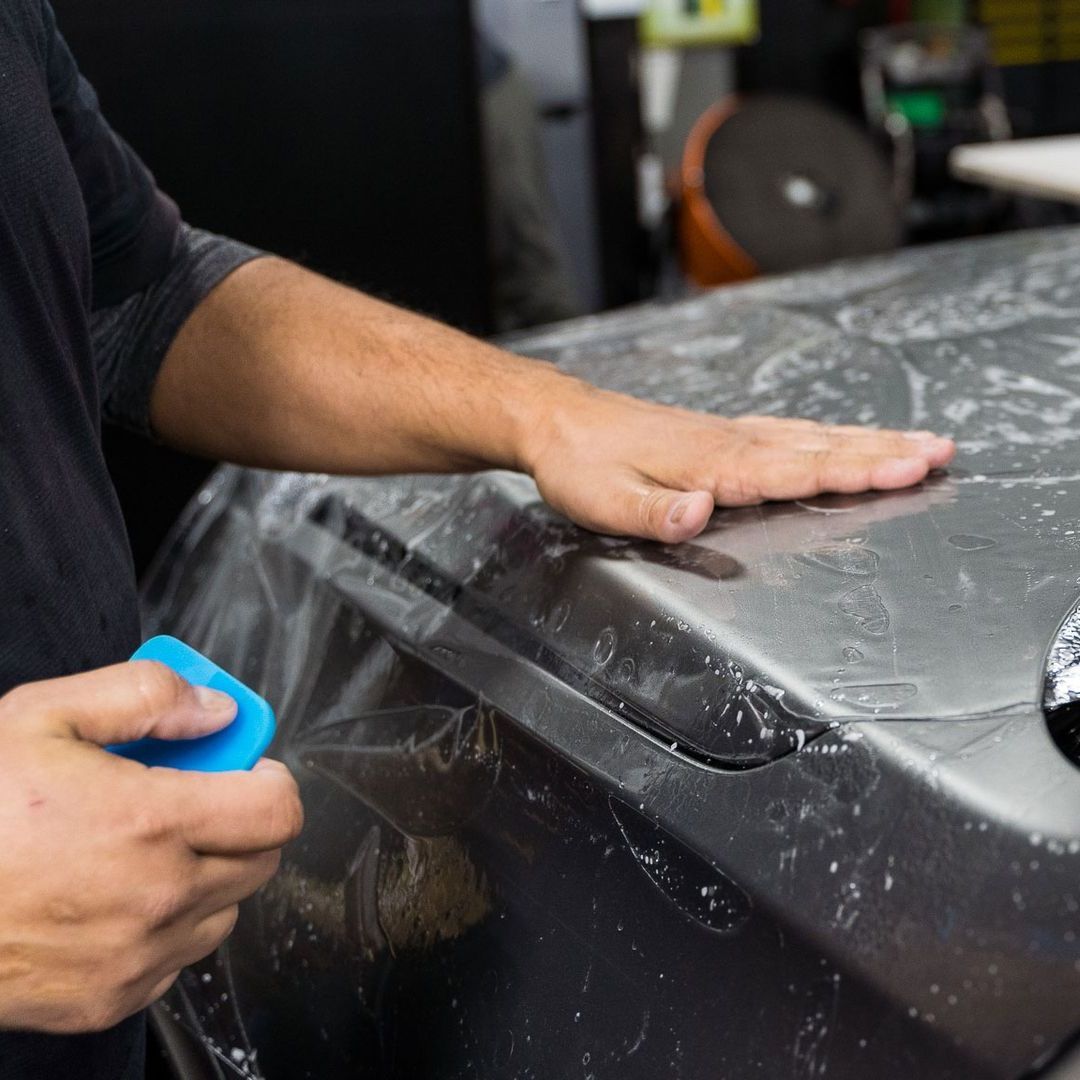 Skilled technician meticulously applying Paint Protection Film to a vehicle's surface.