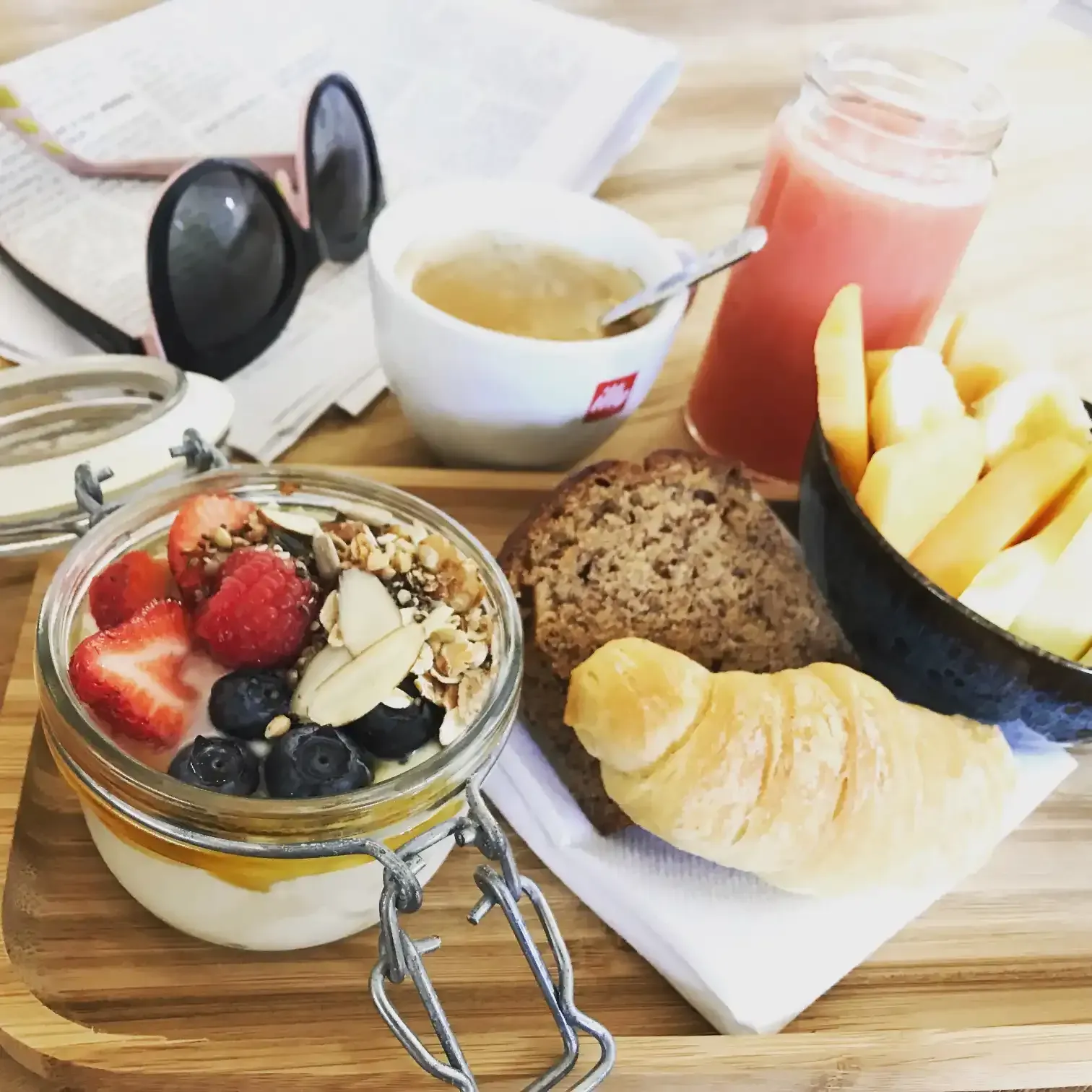 Breakfast tray with yogurt parfait, fruit, bread, croissant, coffee, and juice.
