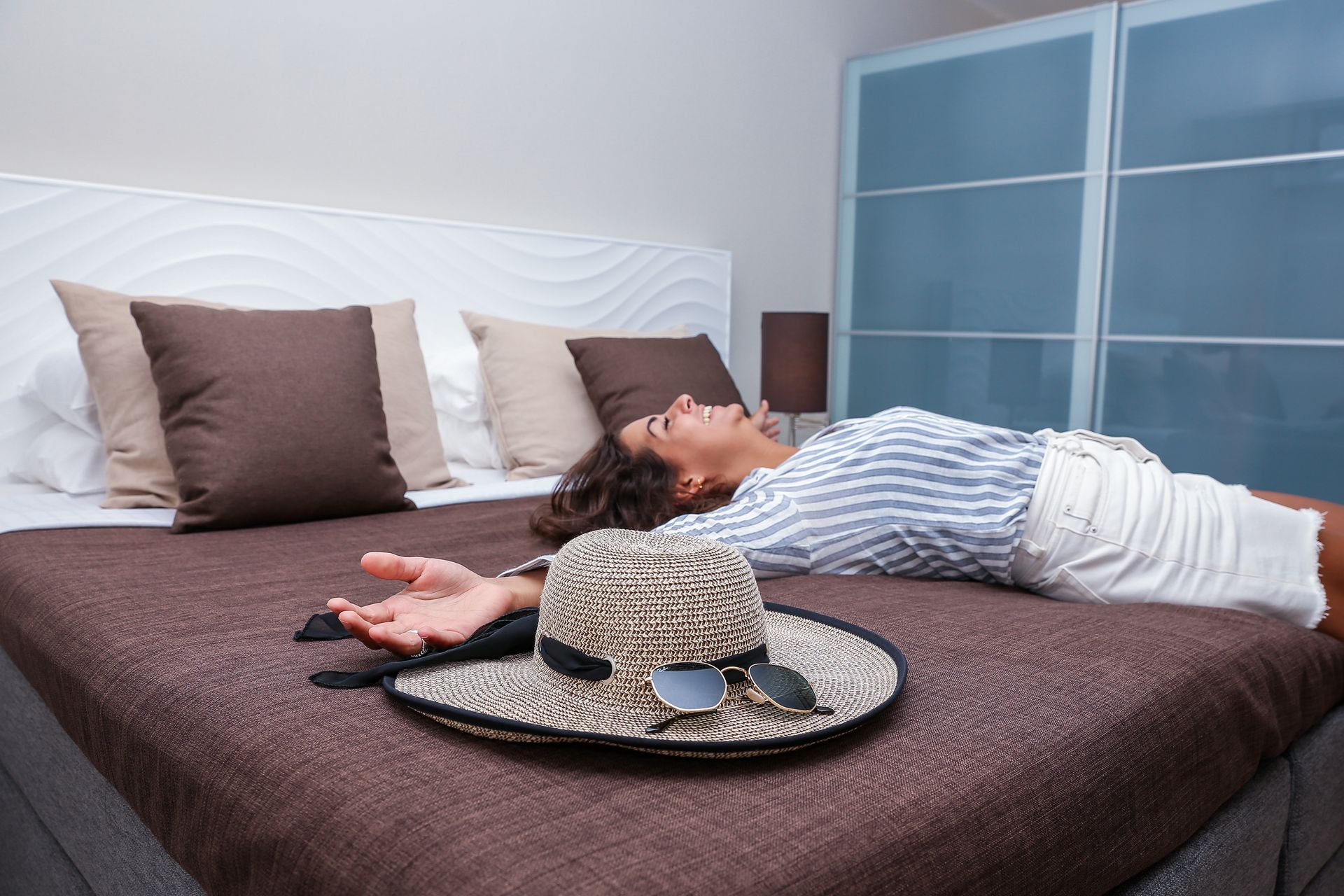 Woman relaxing on a bed, next to a sun hat.