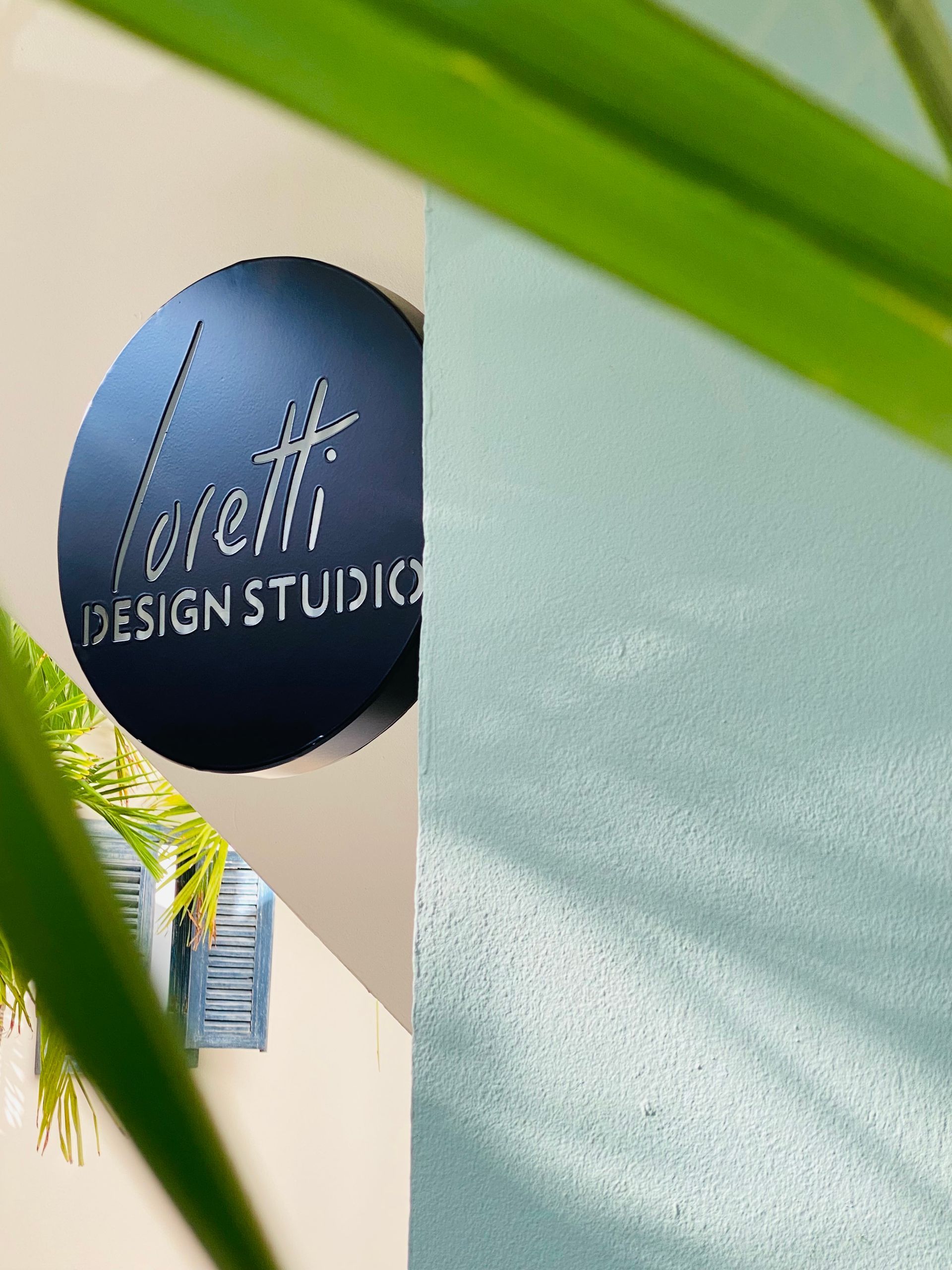 Sign for Loretti Design Studio, blue circle with white script, on a white wall.