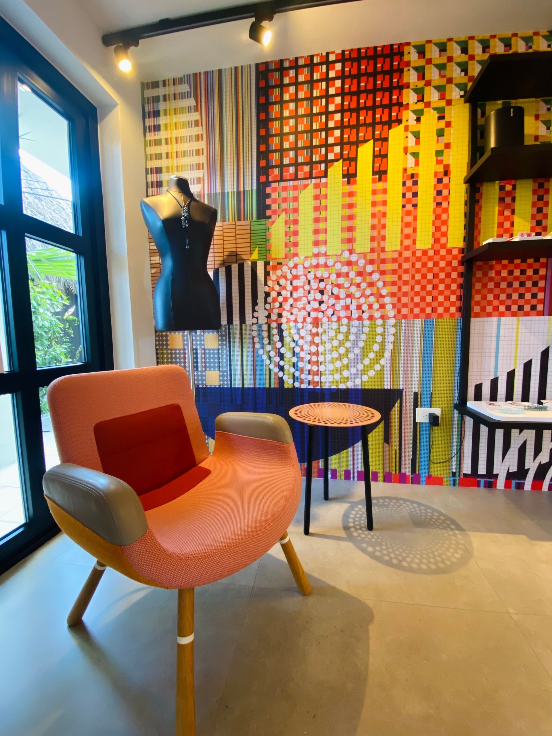 Modern interior with colorful wall art, an orange armchair, small table, and dressmaker's form.