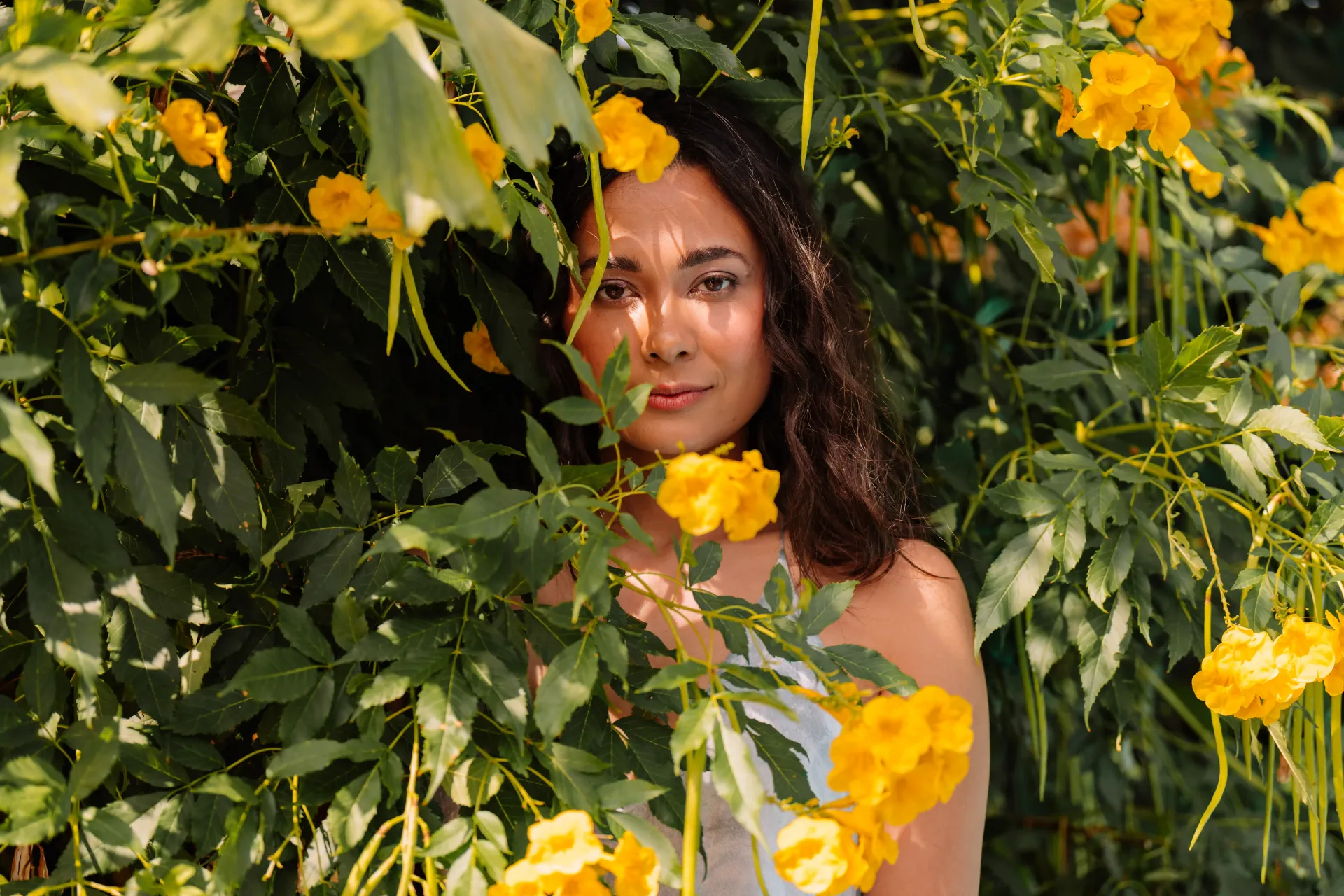 Woman peeking through yellow flowers and green leaves.