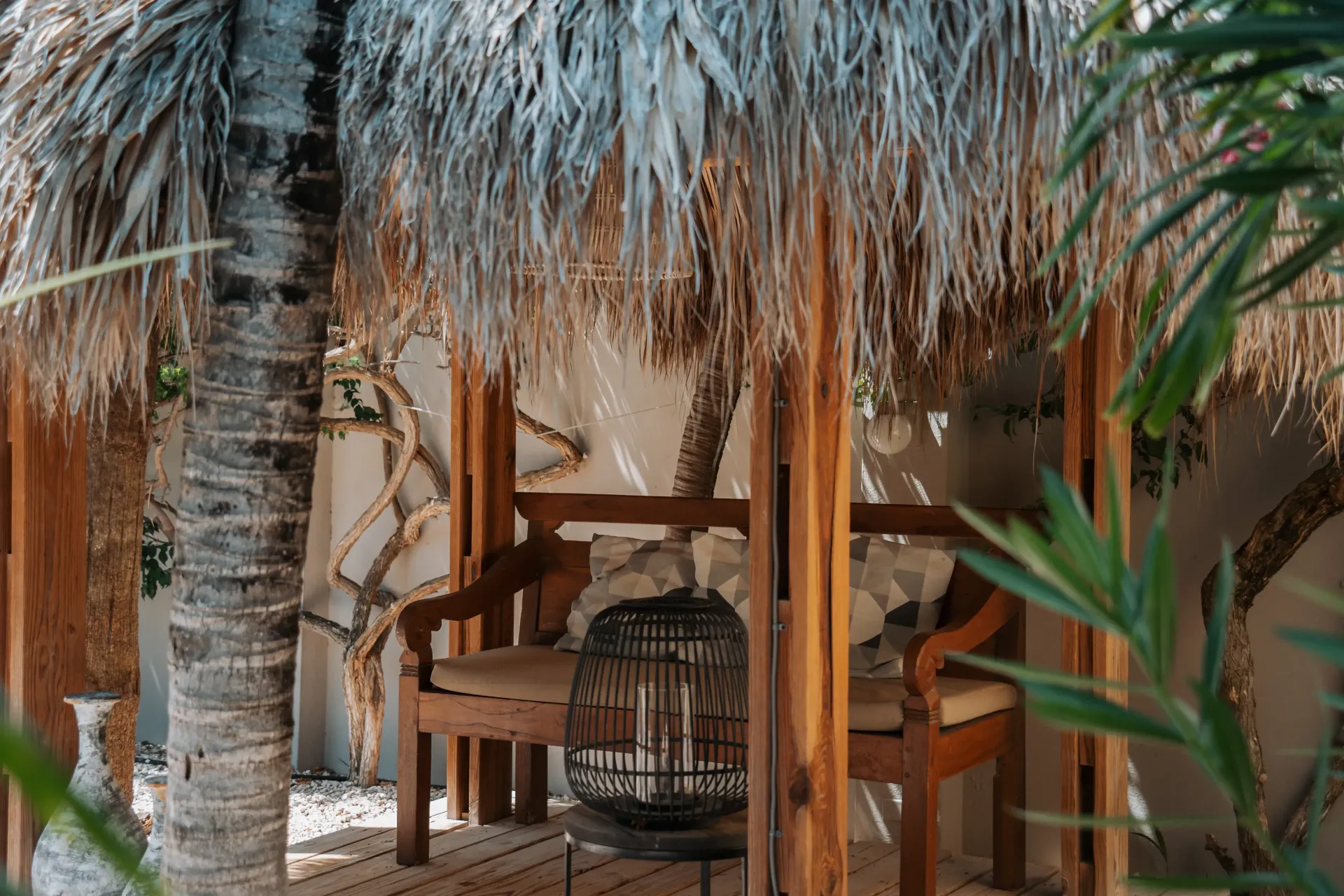 Wooden bench under a thatched roof structure, in a tropical setting.