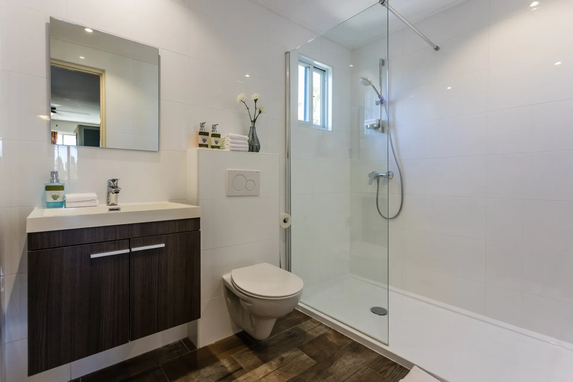 Modern bathroom with a glass shower, toilet, and vanity with dark brown cabinets.