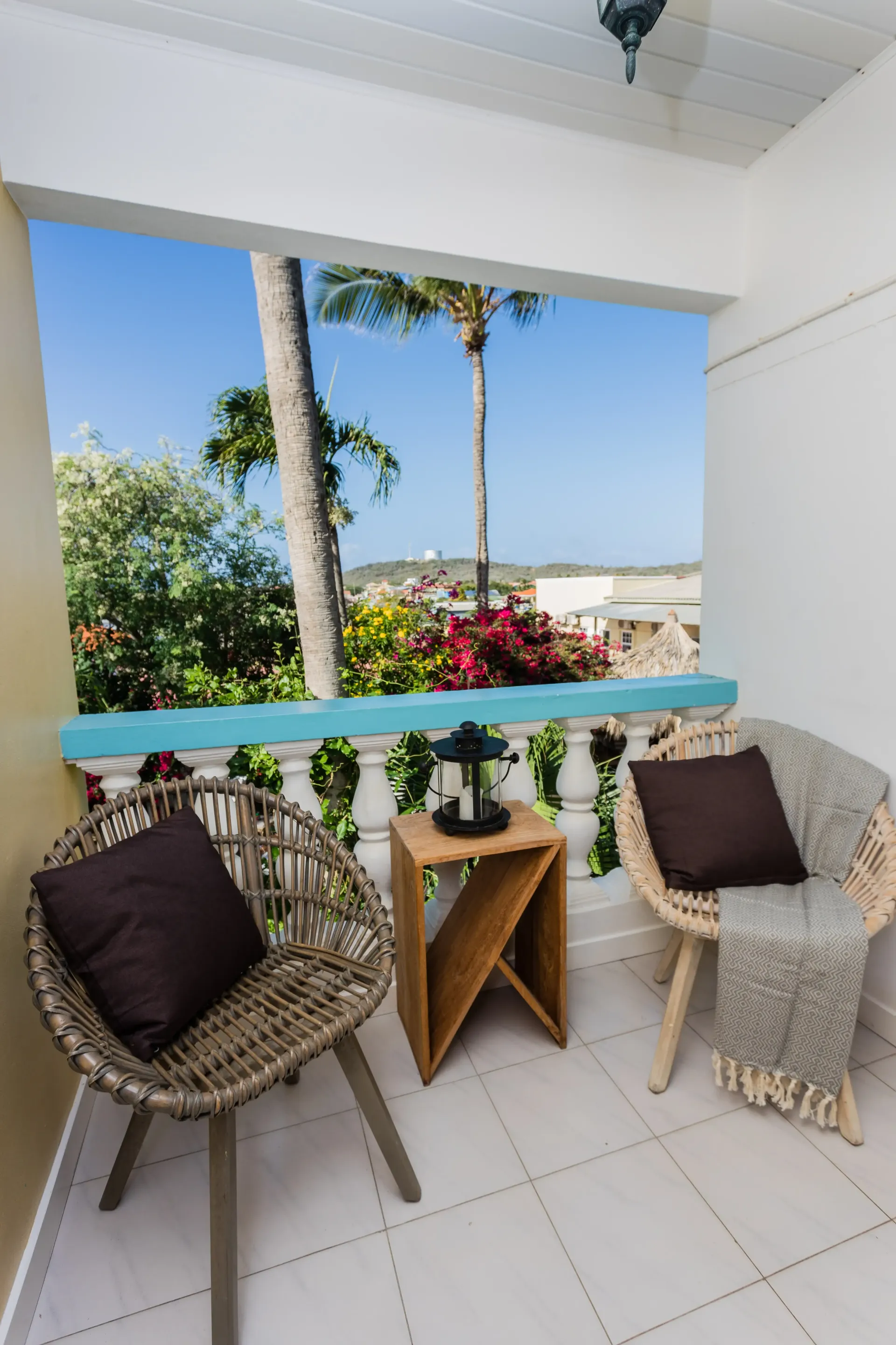 Balcony with wicker chairs, small table, and a view of trees and sky.