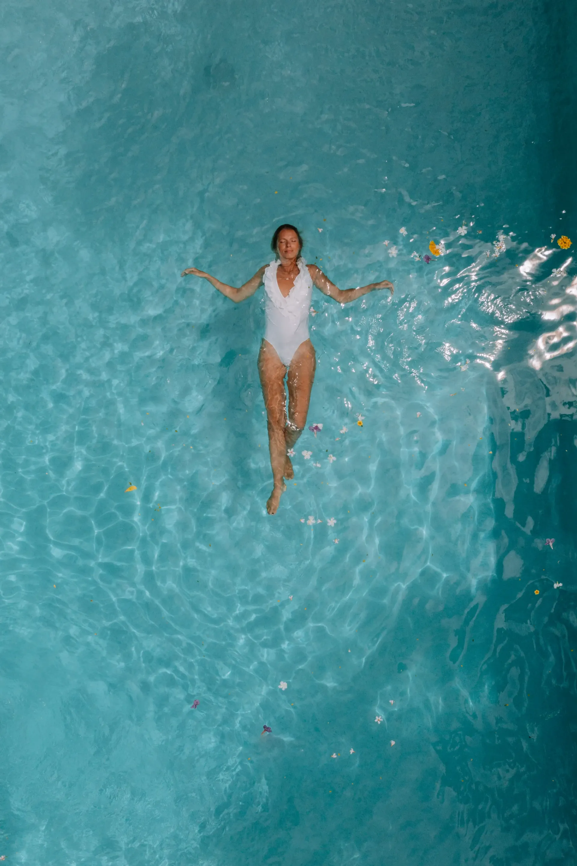 Woman in white swimsuit floating in a clear blue swimming pool, arms outstretched.