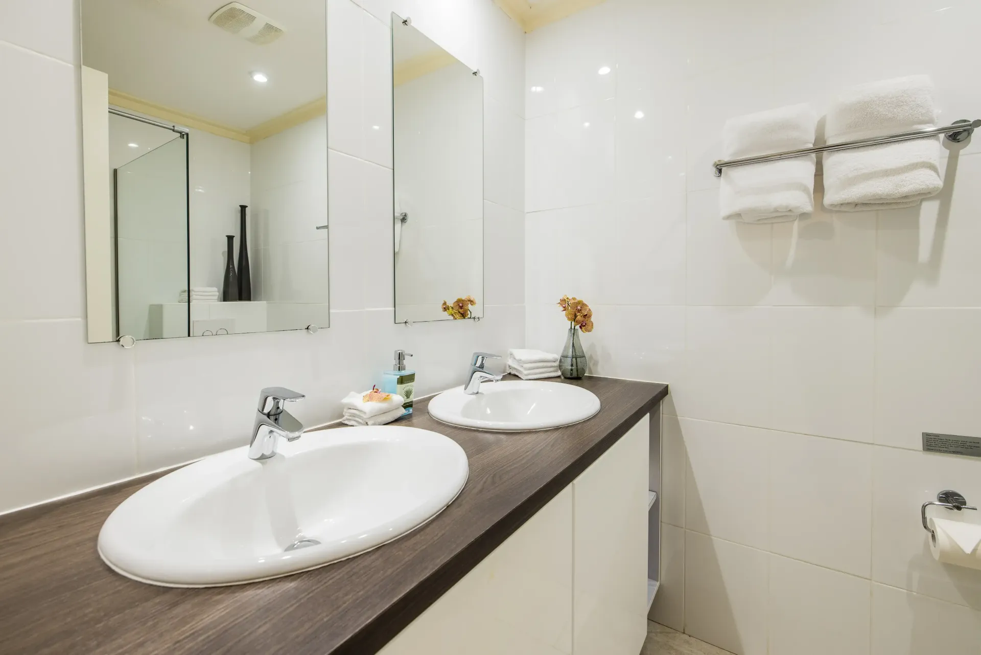 Bathroom with two sinks, two mirrors, and a towel rack with white towels.