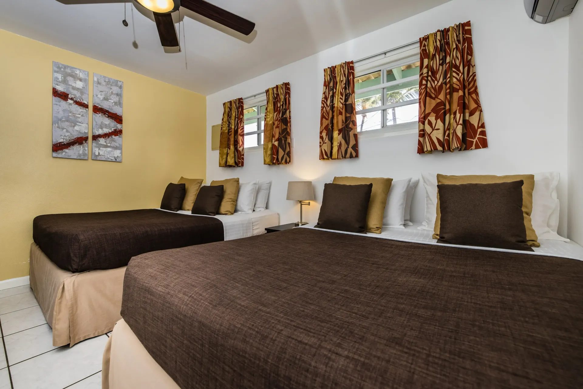 Bedroom with two beds, brown and beige accents, yellow and white walls, windows, and ceiling fan.