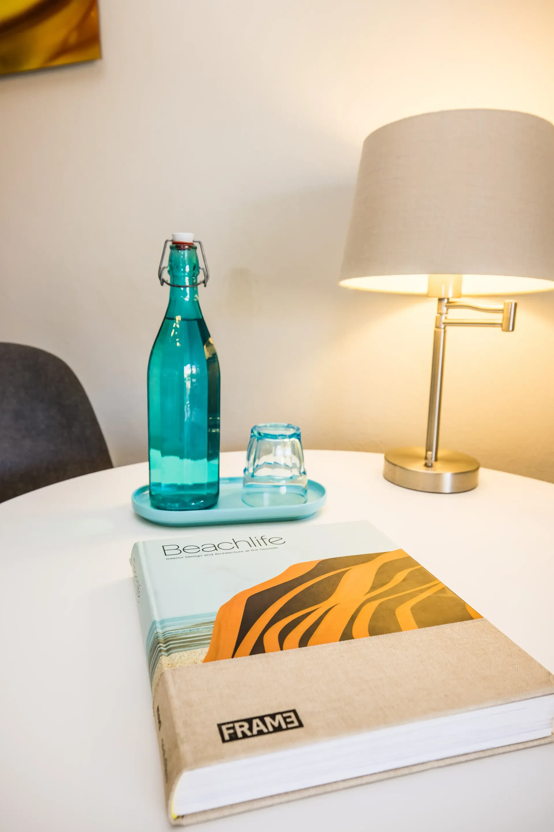 A bedside table with a blue water bottle, glass, lamp, and book.