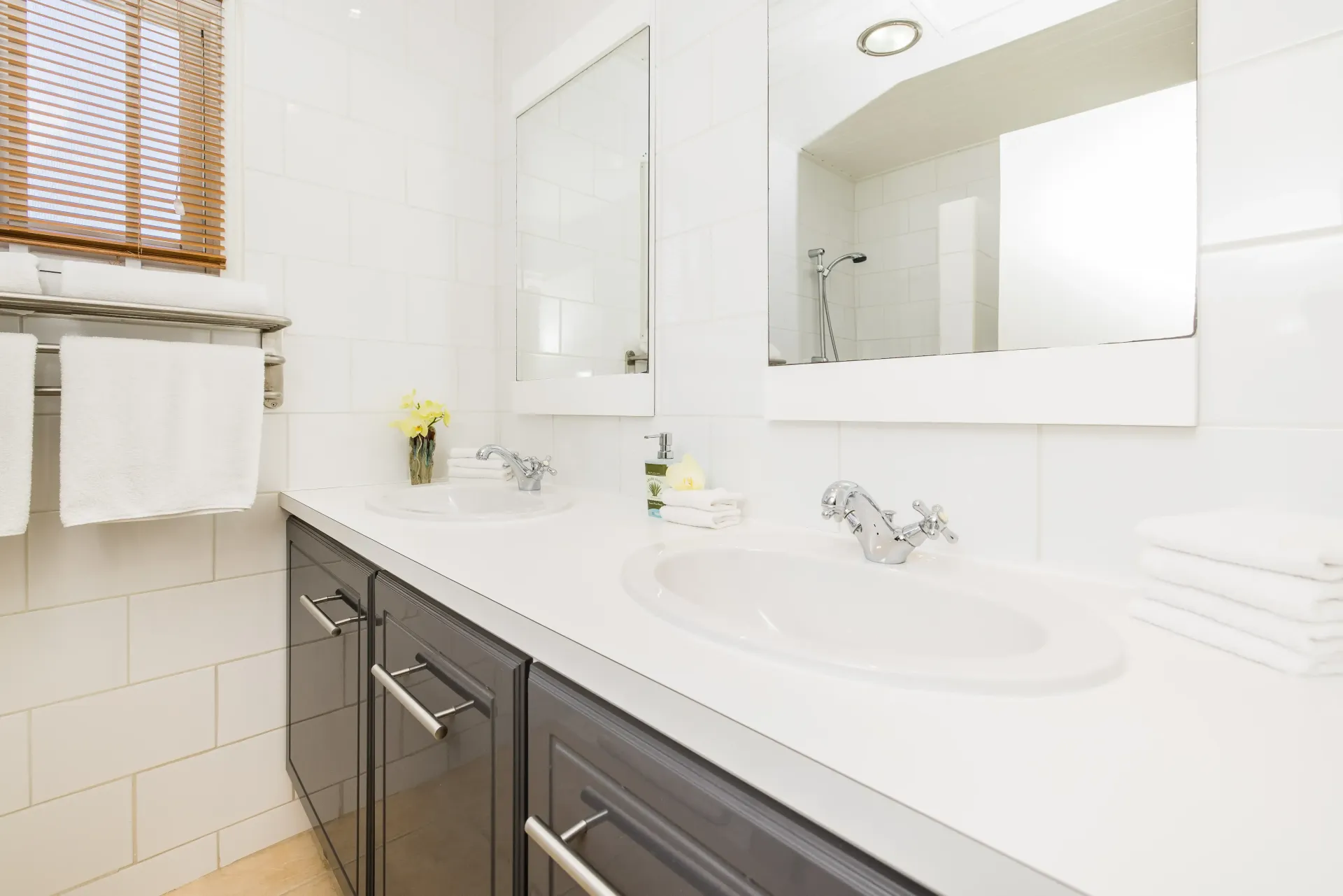 Bathroom with white countertop, dark gray cabinets, two sinks, and a large mirror.