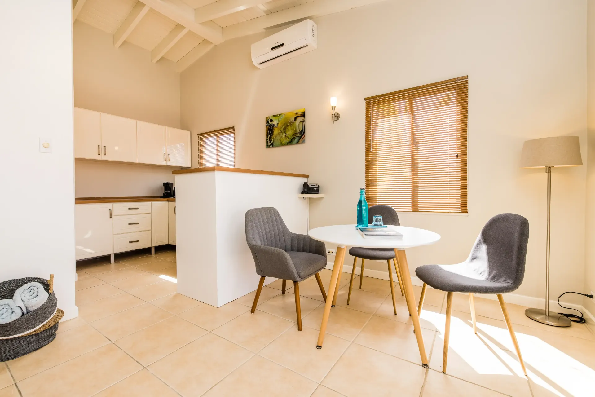 A bright, open-plan kitchen and dining area with a round table and three gray chairs.