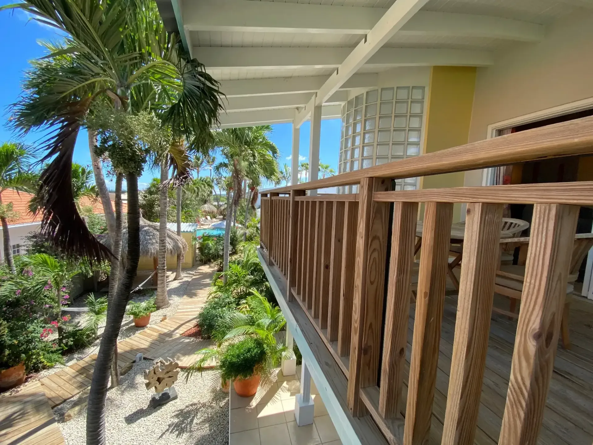 Wooden balcony overlooking lush tropical foliage and pathway. Blue sky visible.