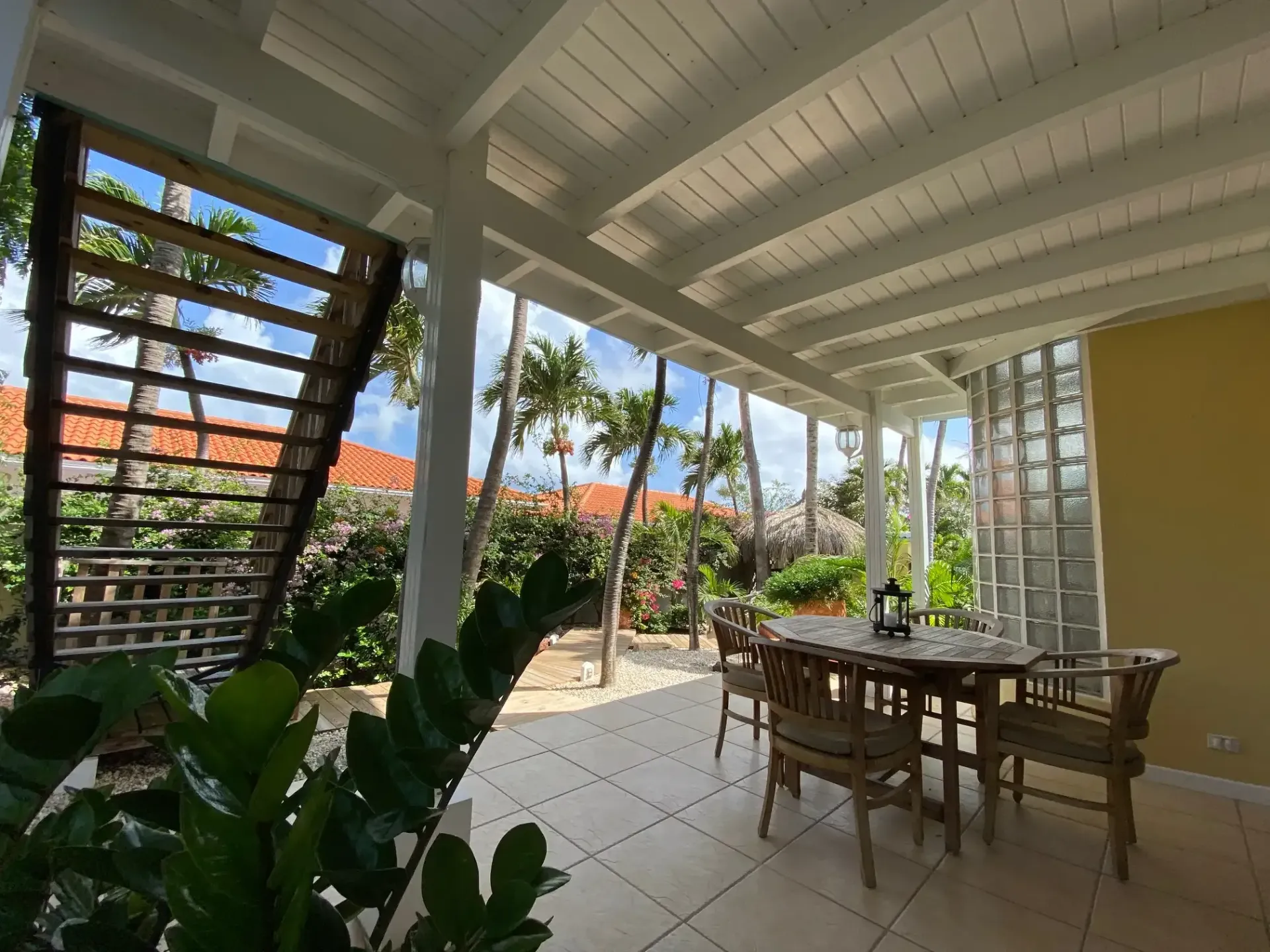 Covered outdoor patio with a dining table, stairs, and tropical greenery.