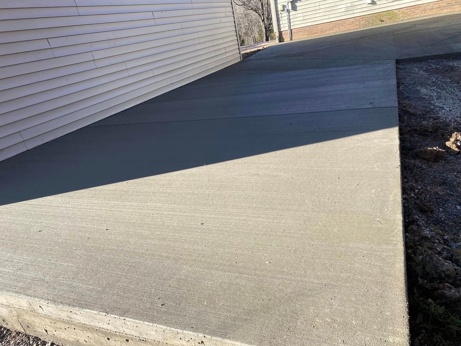 Martinez Construction | A concrete walkway leading to a house with a white fence in the background.