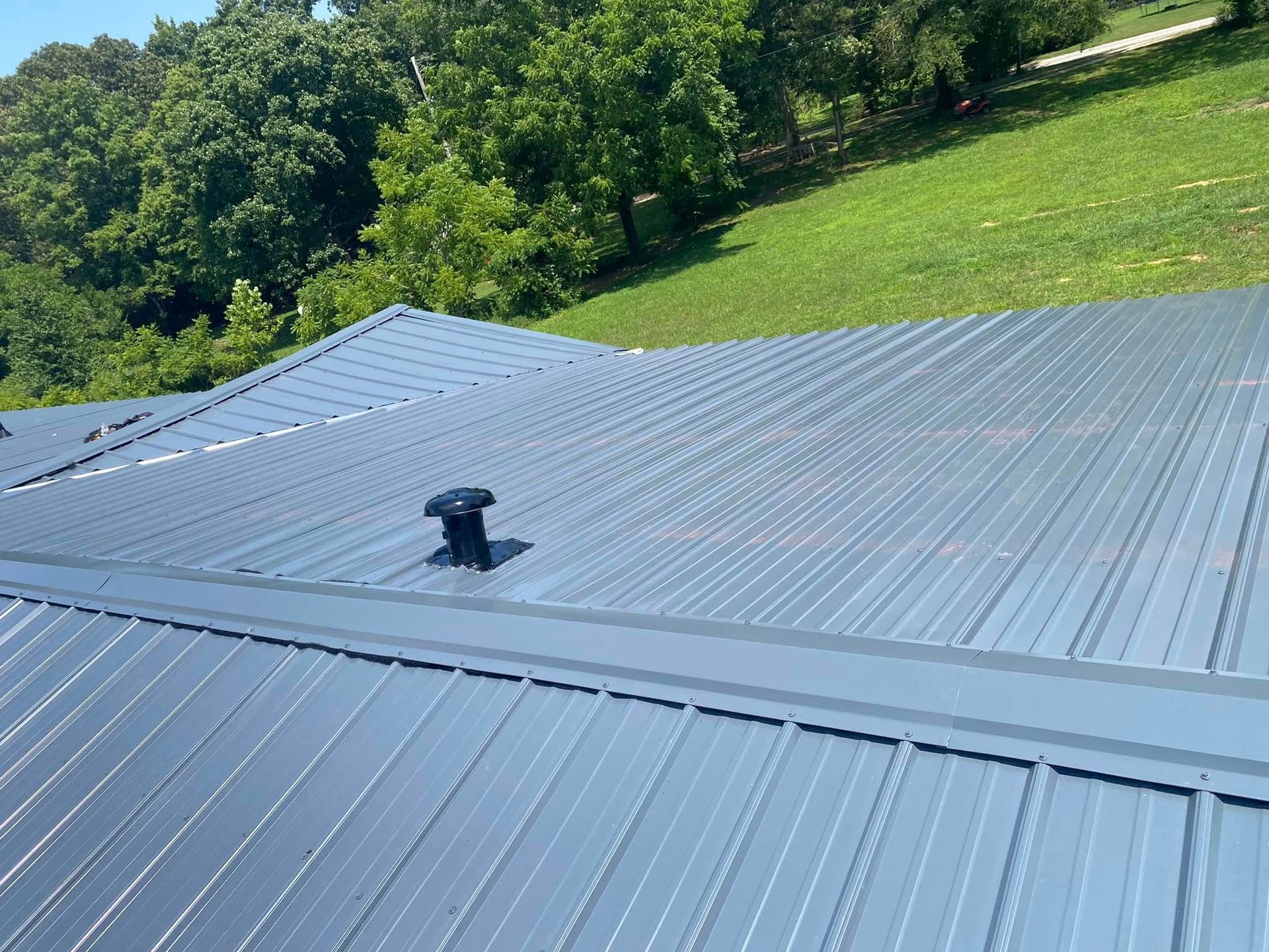 Martinez Construction | A roof with a vent on it is surrounded by trees and grass.