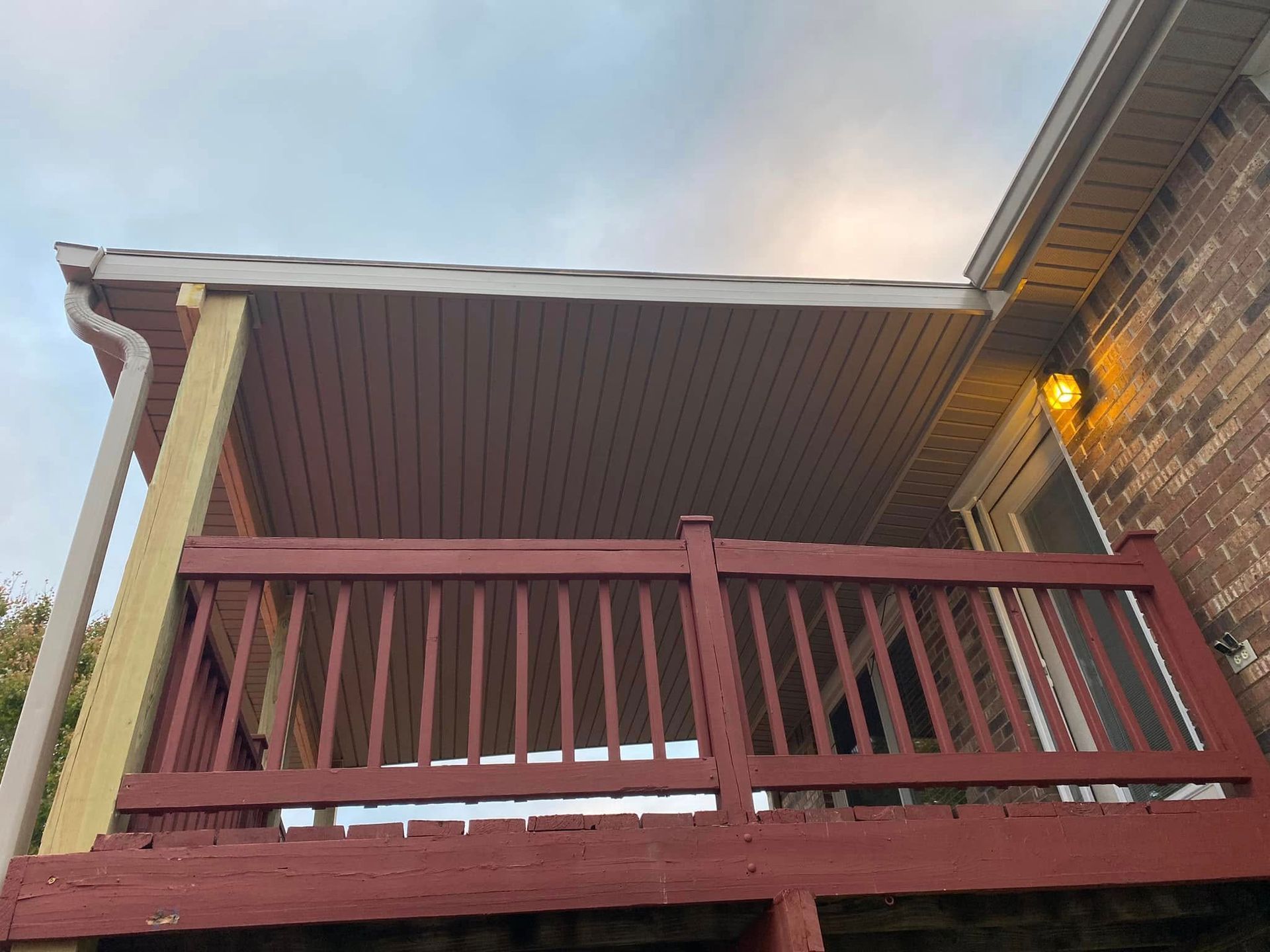 Martinez Construction | A red deck with a roof over it is sitting under a brick house.