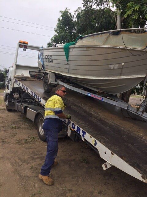 A Man Is Standing Next To A Tow Truck With A Boat On It — Bohle Welding & Trailer Repairs In Bohle, QLD