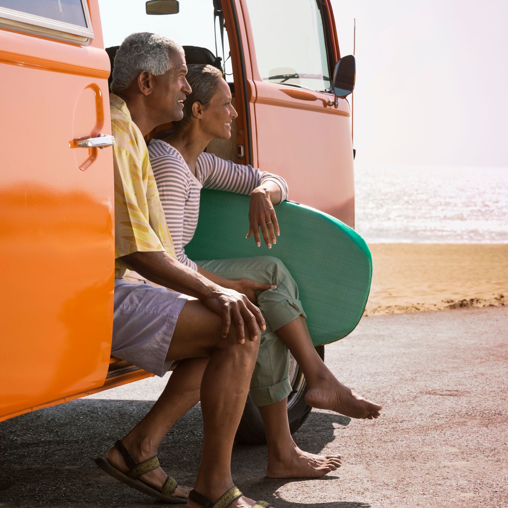 Two people sitting by an orange van at a beach, watching the ocean