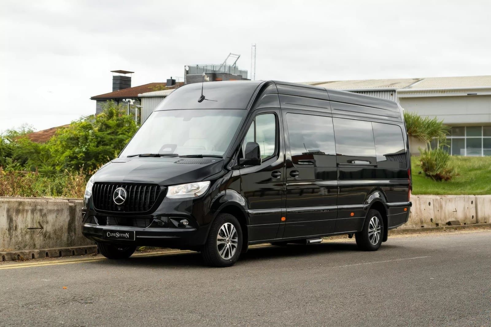 Black van parked on a paved road, facing left, in front of a building, and on a cloudy day.