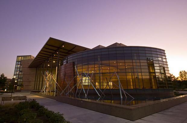 Modern glass and brick building with water feature at sunset.