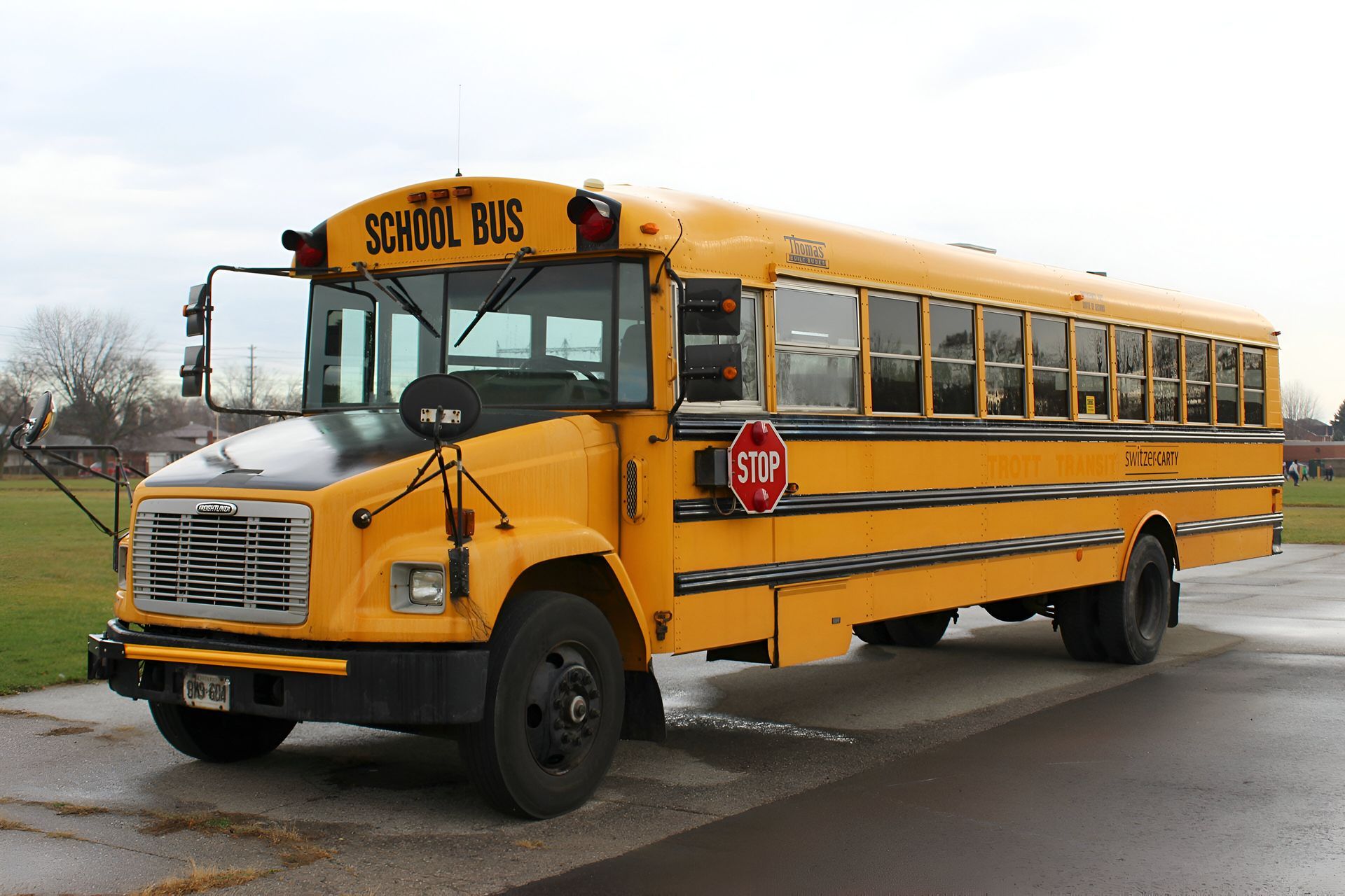 Yellow school bus parked on a paved area, with a stop sign extended, cloudy day.