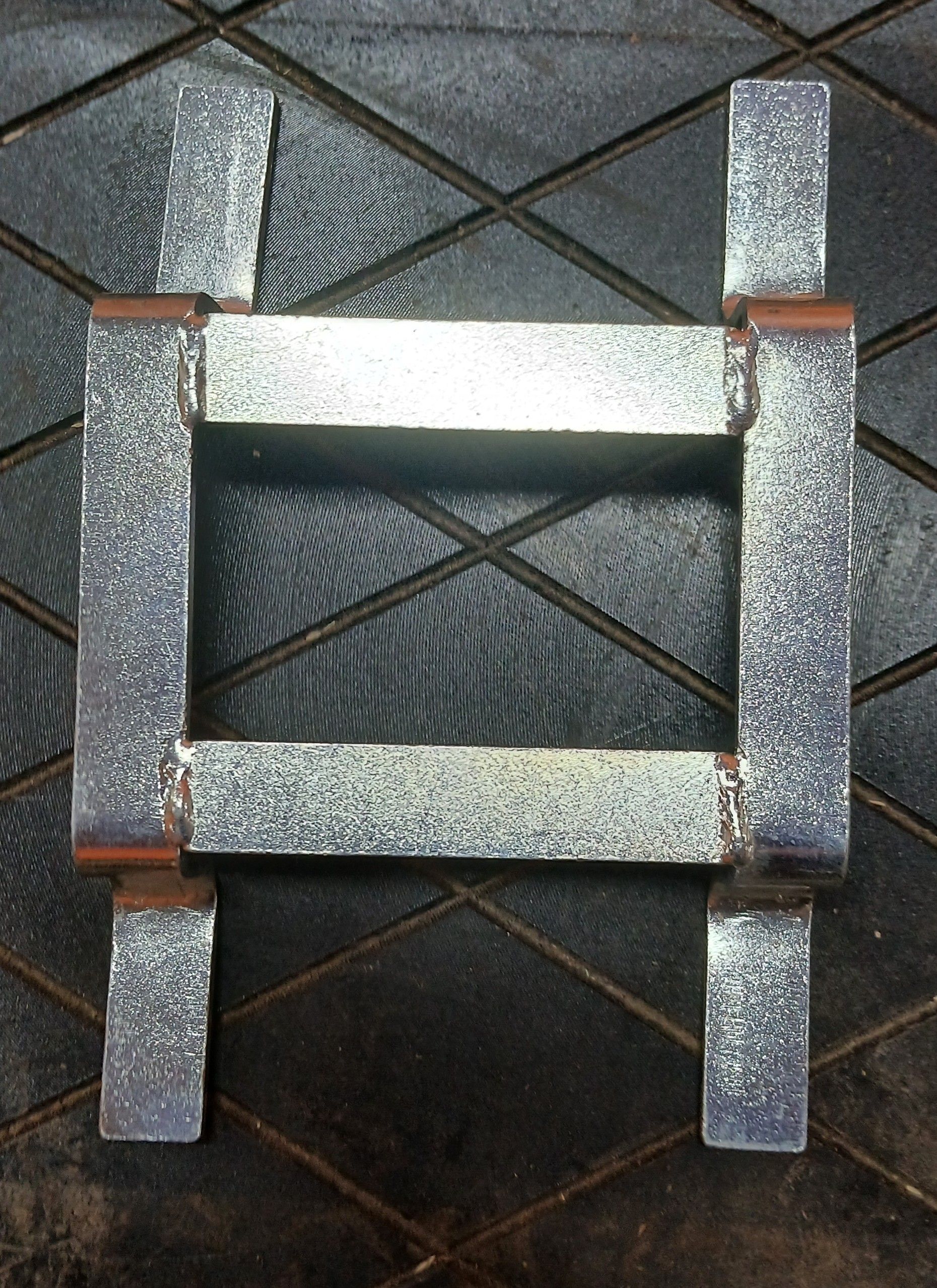 Metal, rectangular frame, likely a fabricated part, on a textured dark surface.