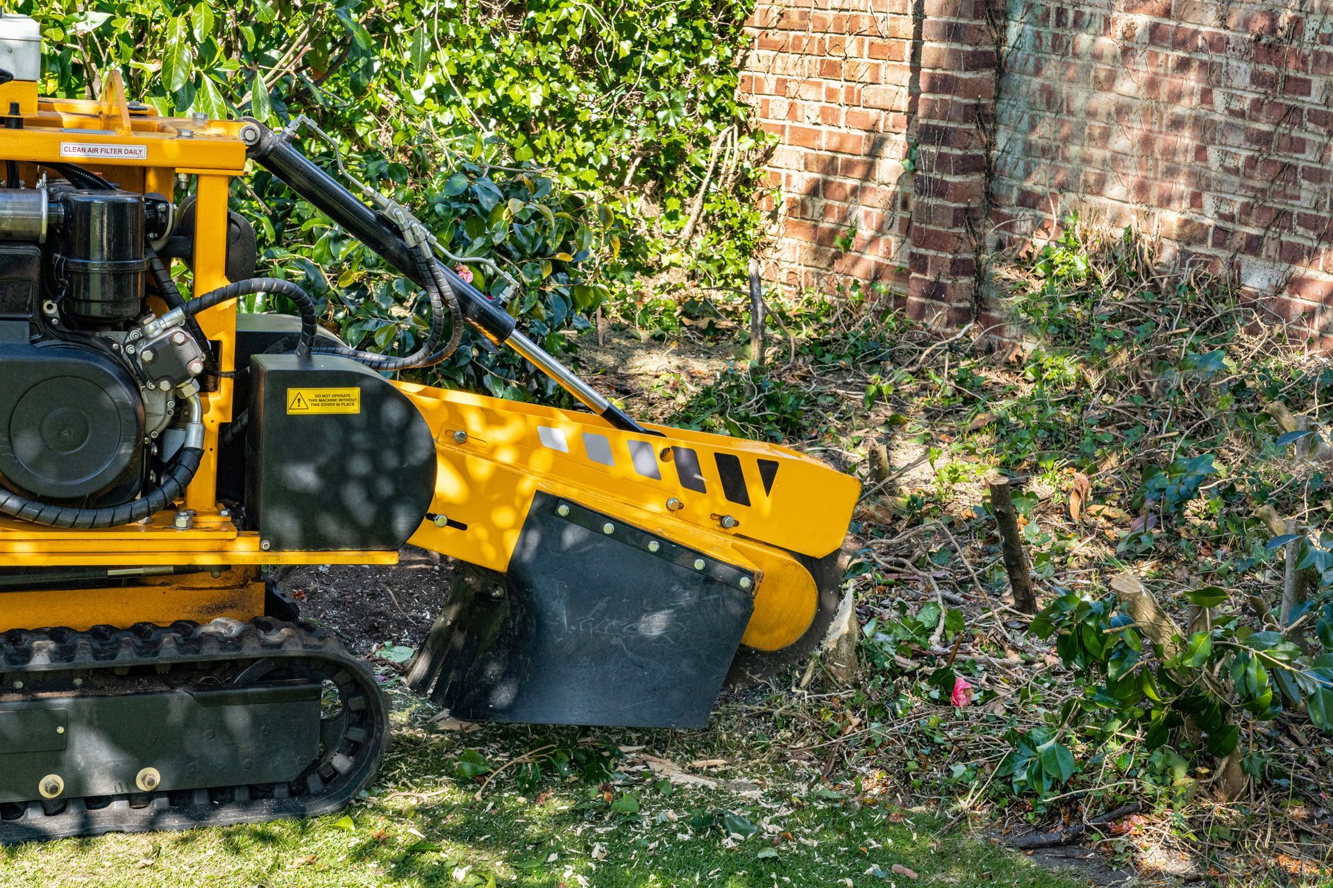 A yellow stump grinder is sitting in the grass next to a brick wall. A yellow stump grinder is sitting in the grass next to a brick wall.