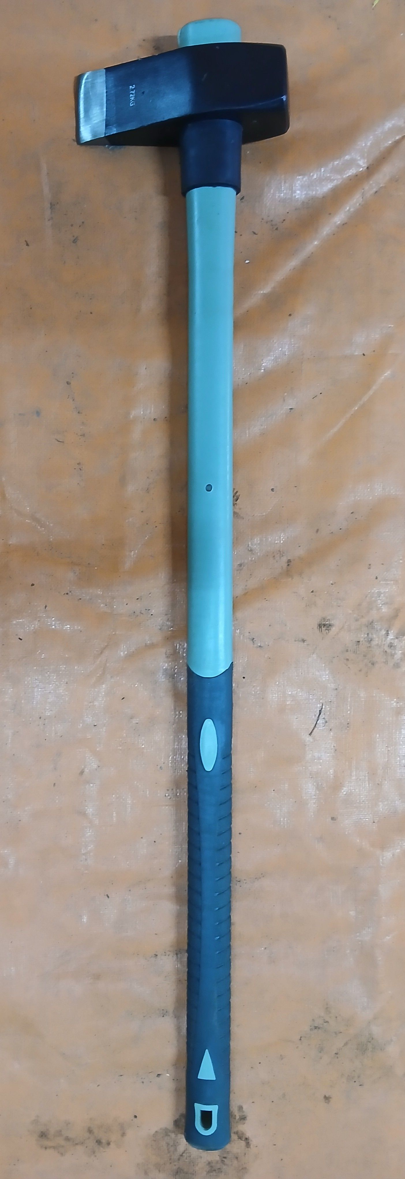 A sledgehammer with a black head and a green and black handle, resting on an orange surface. A sledgehammer with a black head and a green and black handle, resting on an orange surface.