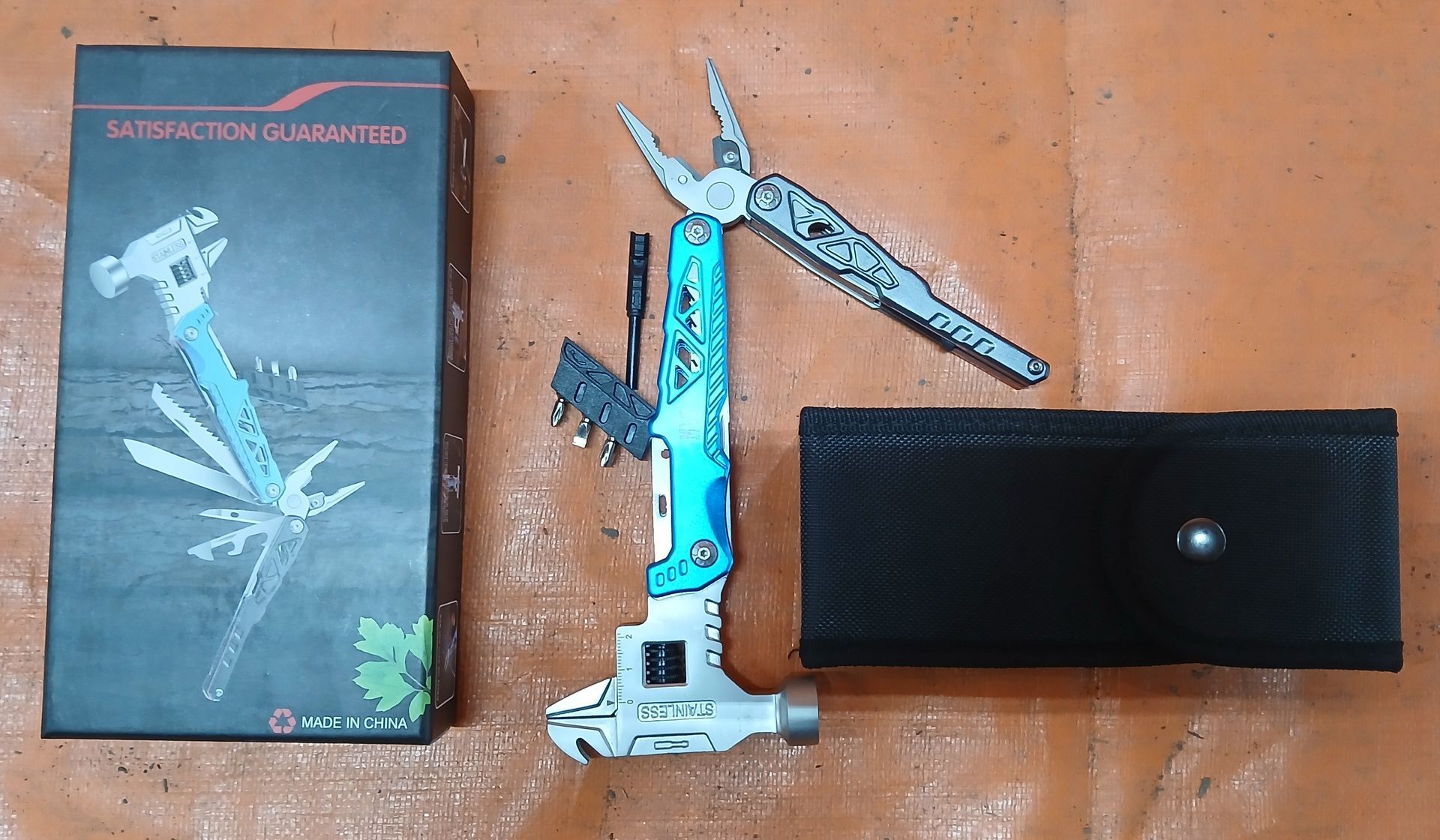 Multi-tool with case and box on a brown surface. The tool is turquoise and silver. The box is black. Multi-tool with case and box on a brown surface. The tool is turquoise and silver. The box is black.