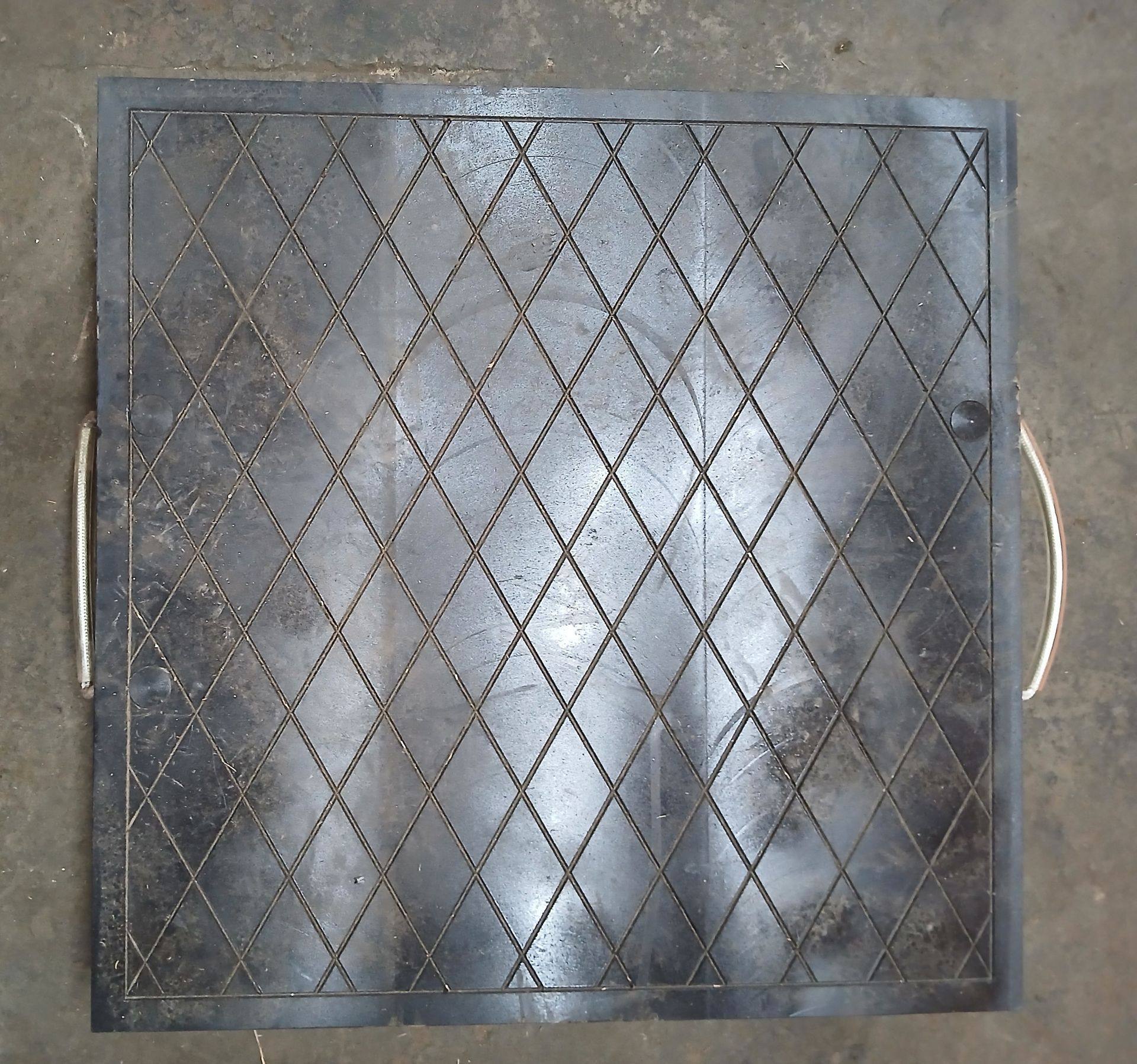 Square black metal grate with diamond pattern and handles.