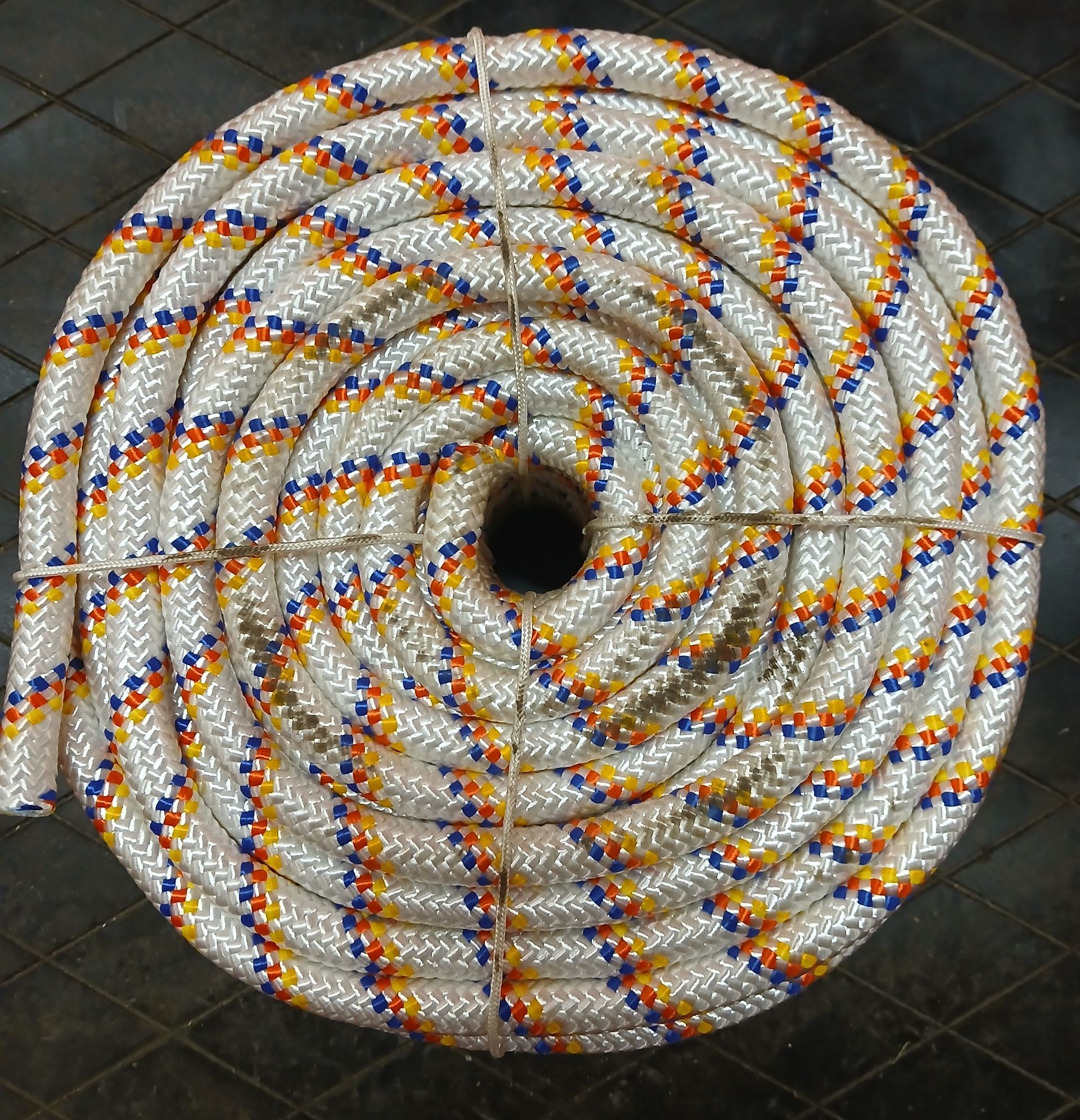 Coiled rope with white, orange, blue, and yellow strands, secured with twine. Coiled rope, white with orange, blue, and yellow flecks, secured with twine.