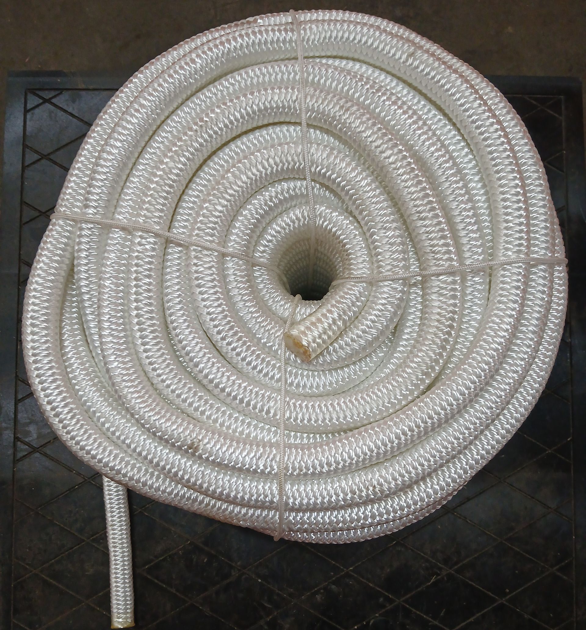 Coiled white rope bound with thin twine, lying on a dark surface. Coiled white rope bound with thin twine, lying on a dark surface.