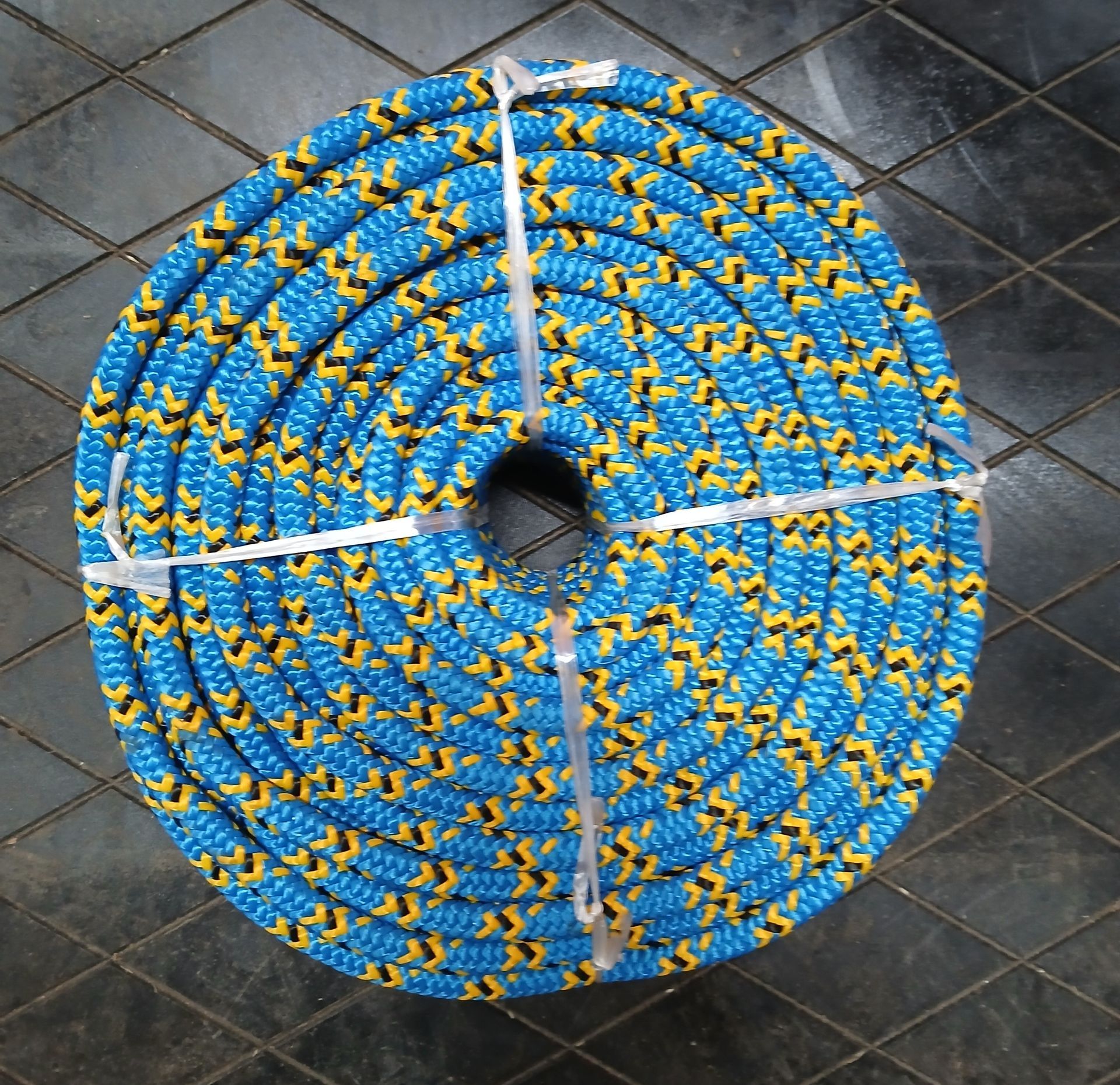 Coiled blue and yellow rope secured with white ties, on a black and gray tiled surface. Coiled blue and yellow rope secured with white ties, on a black and gray tiled surface.